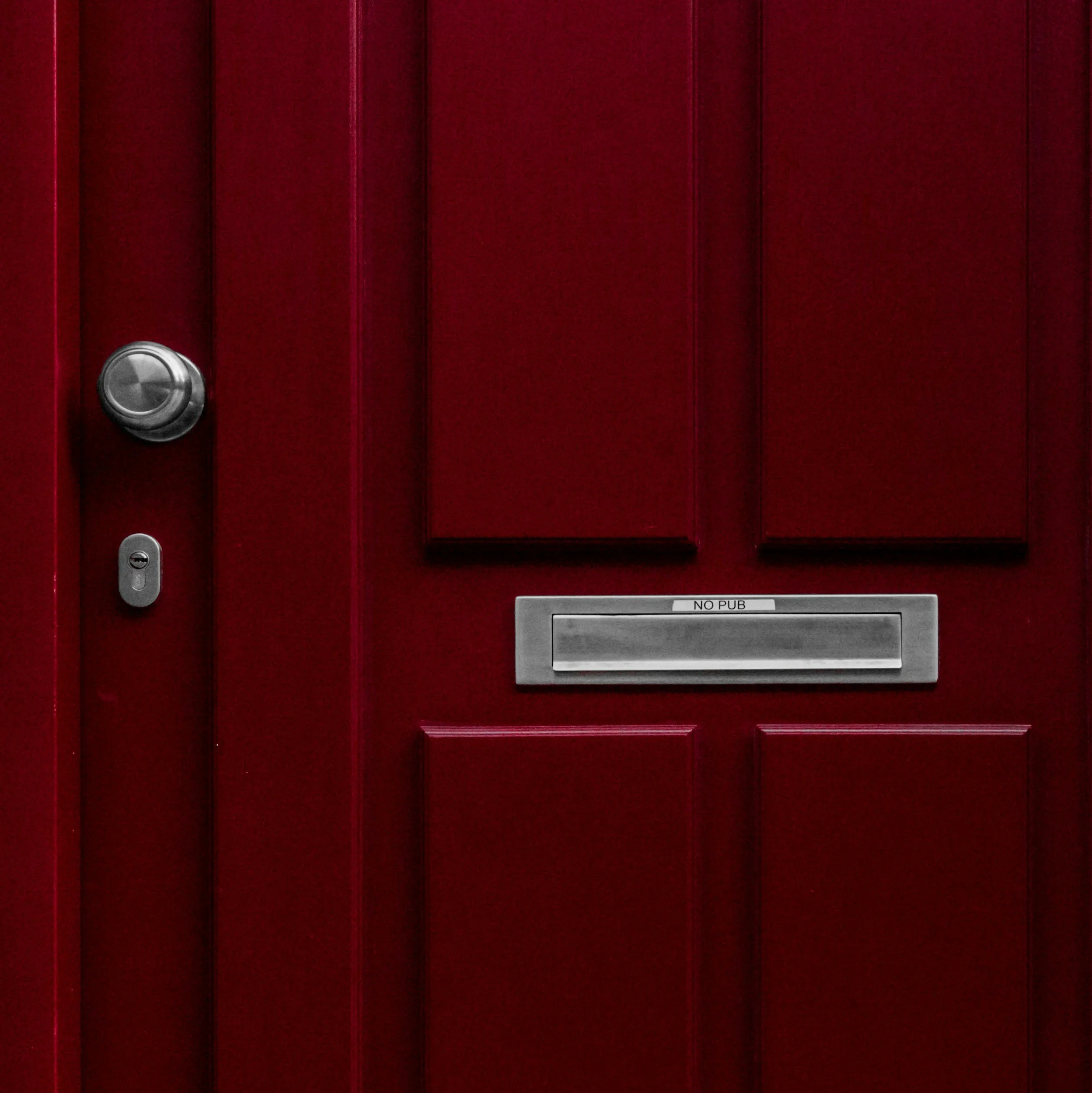 Red front door with silver doorknob, keyhole, and mail slot with a label 'NO PUB'.