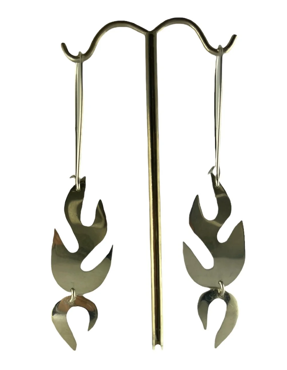 Silver earrings shaped like flames hanging from hooks on a gold display stand.