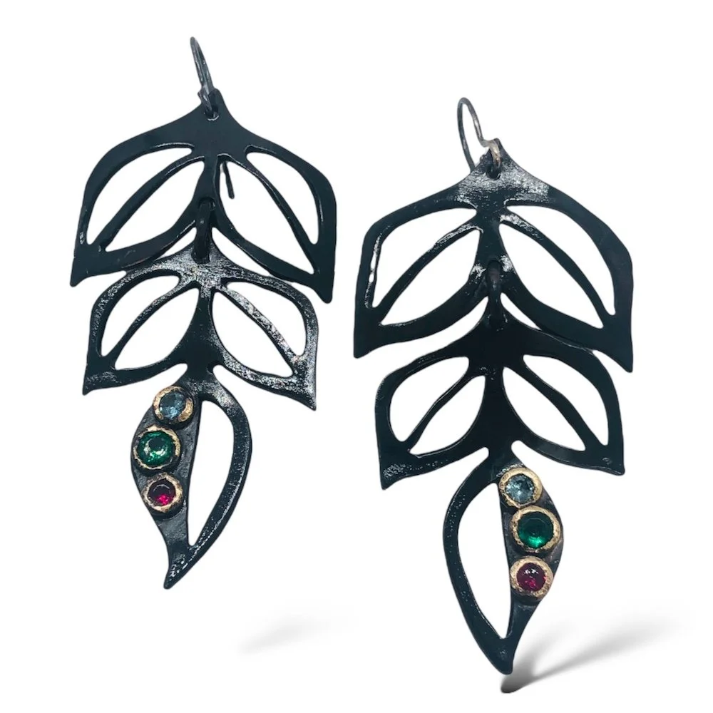 Black metal leaf-shaped earrings with colorful gemstones at the bottom.