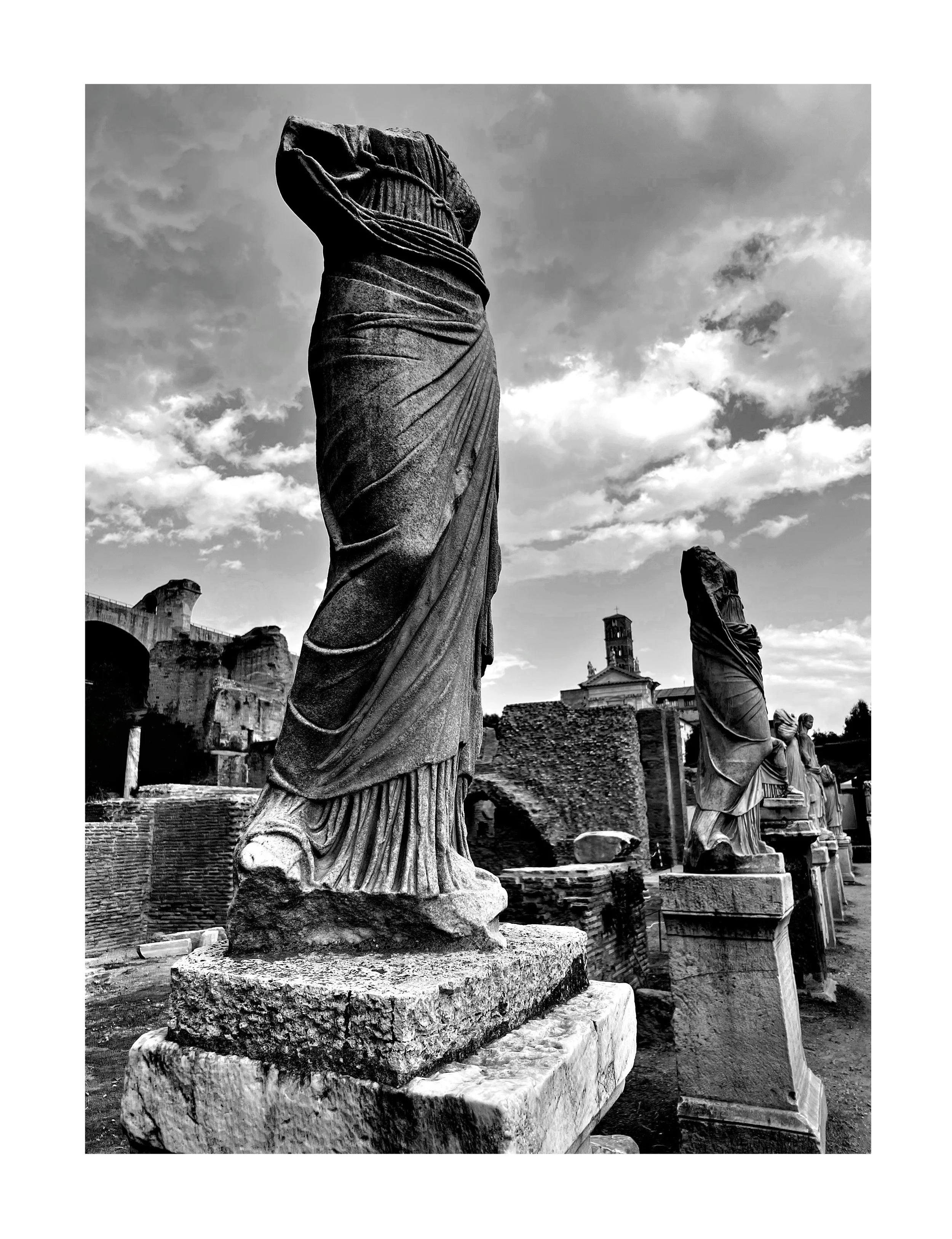 Statues antiques en ruines romaines avec un ciel nuageux en arrière-plan.