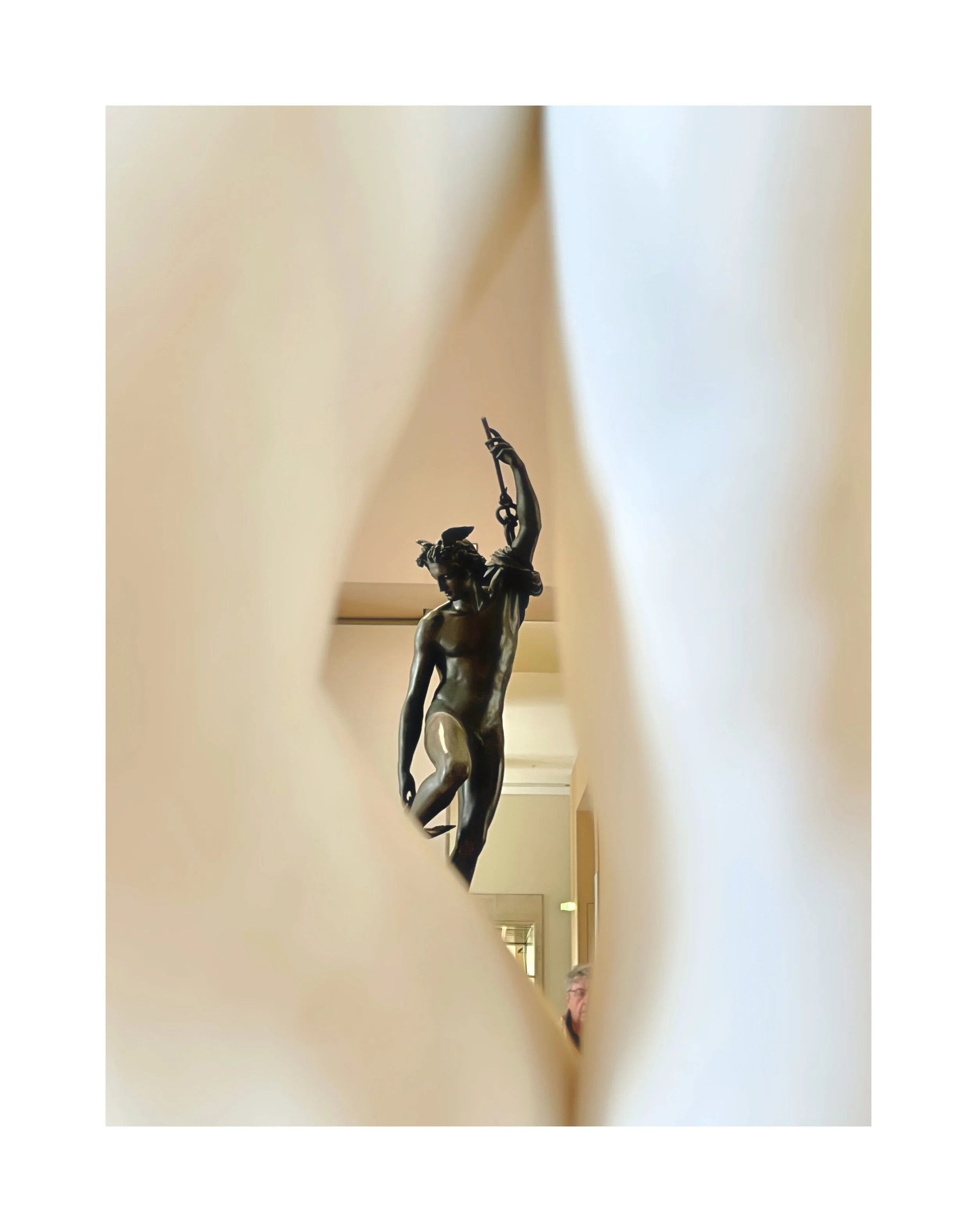 Statue d'un homme nu, vu à travers une ouverture dans un mur. La statue tient un arc et une flèche, représentant probablement une figure mythologique.