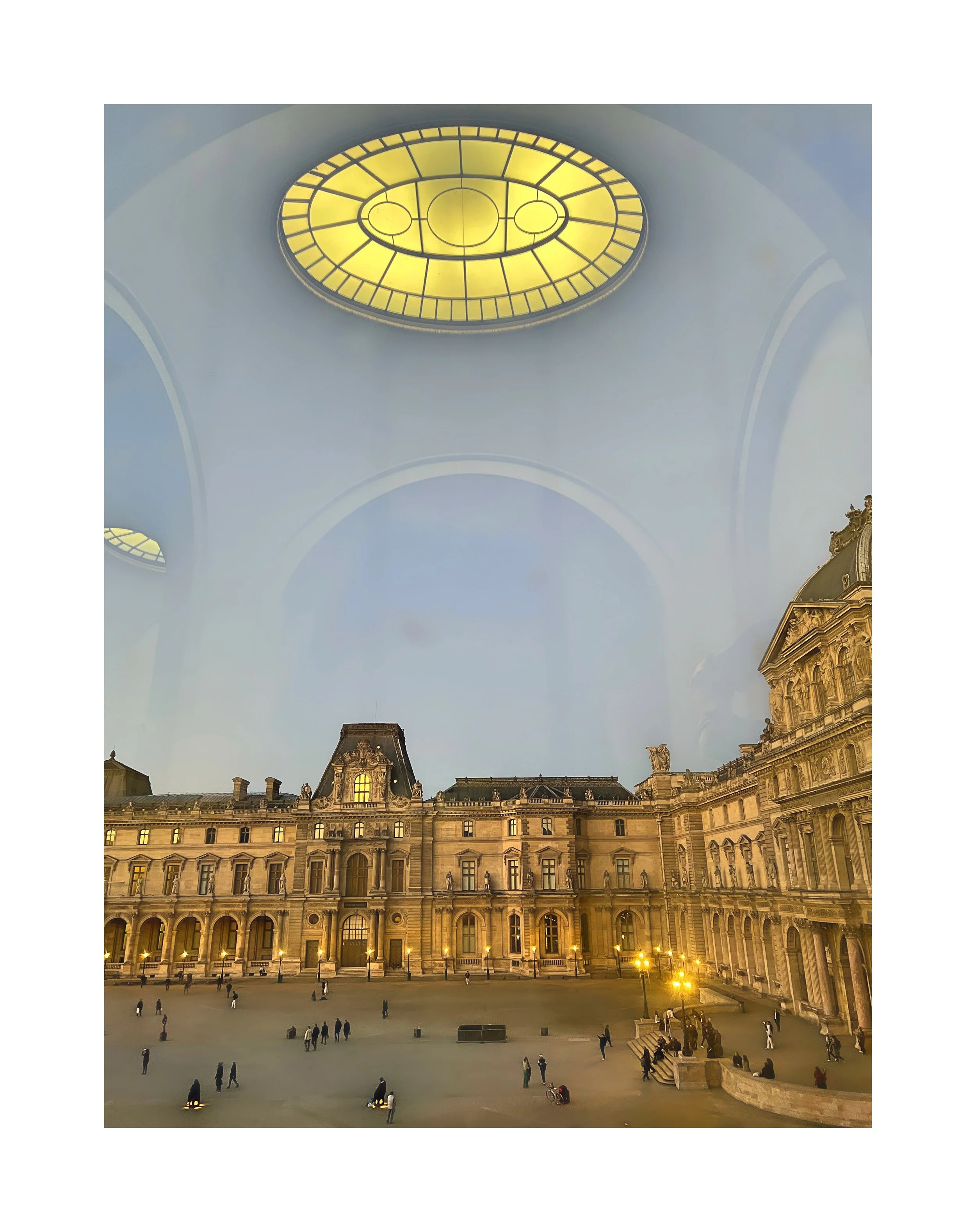 Vue intérieure d'une cour de bâtiment historique avec un plafond en verre jaune au-dessus, et des personnes et lampadaires éclairant la place pavée.