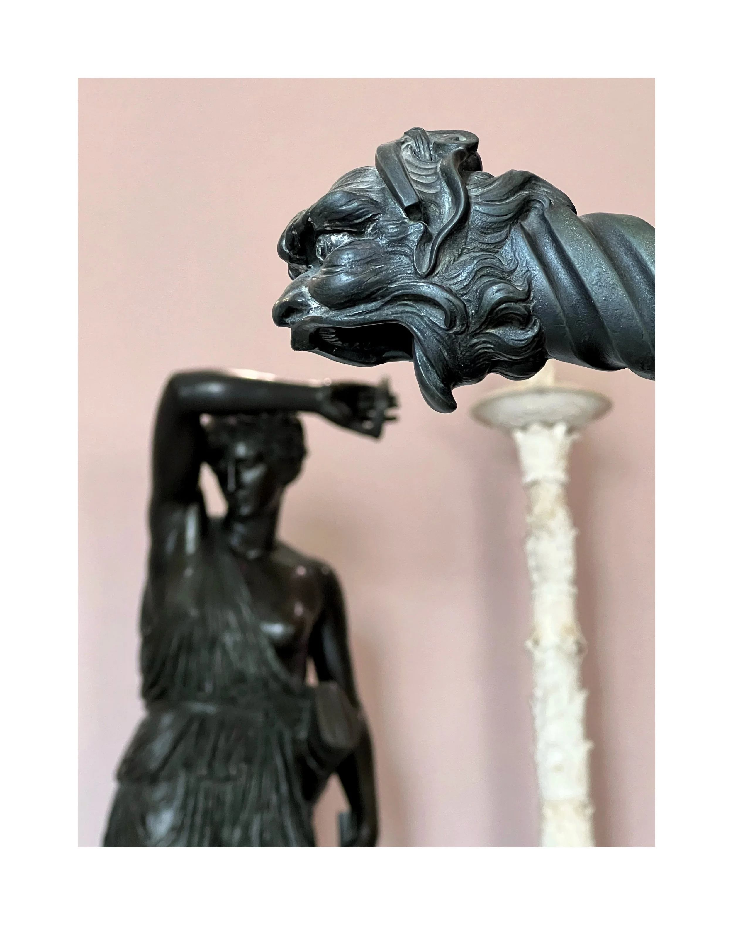 Sculptures en bronze représentant un lion et une femme, la femme se couvre les yeux du bras droit, fond rose en arrière-plan.