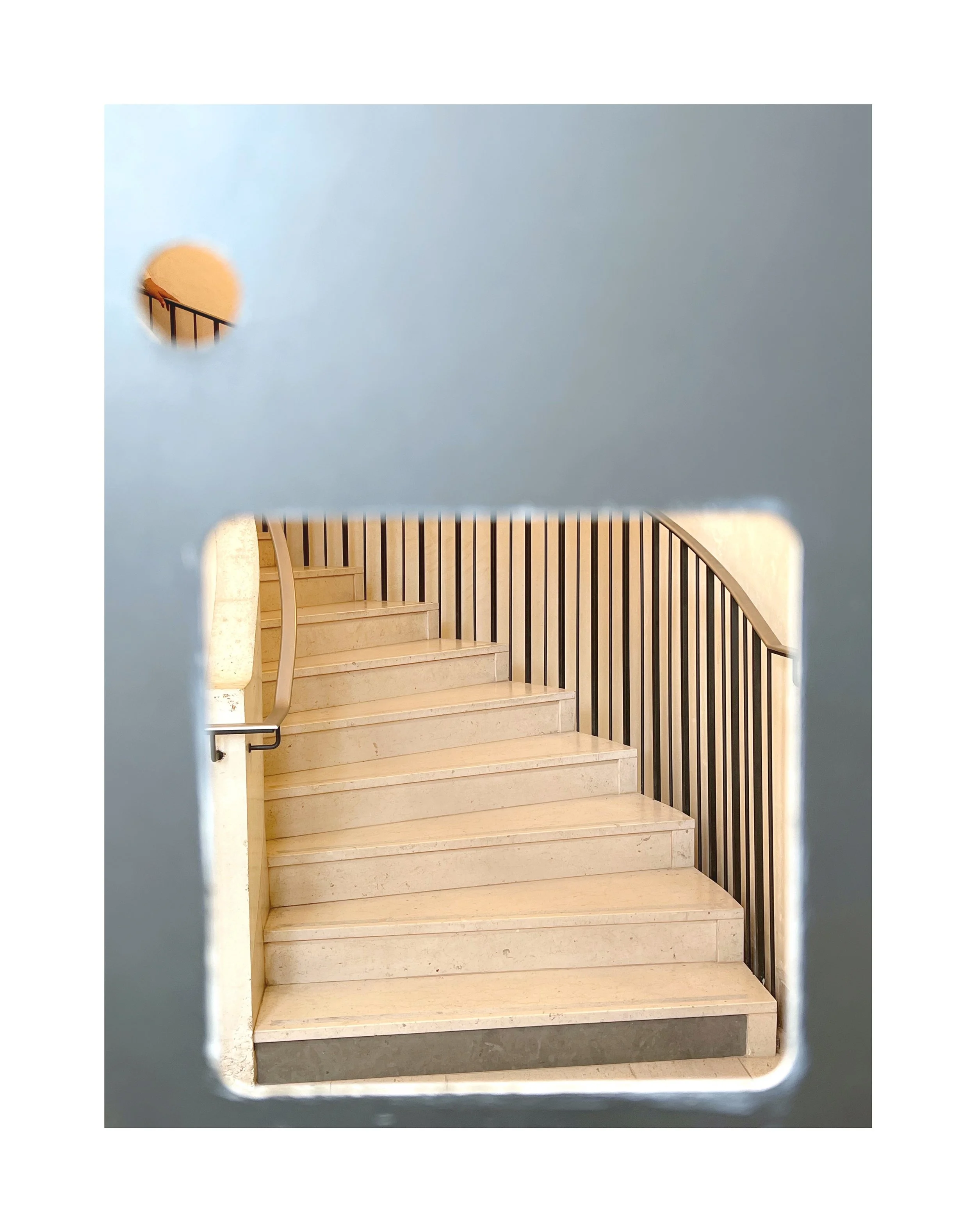 Escalier en marbre vu à travers une ouverture dans une paroi avec une barrière en bois à droite.