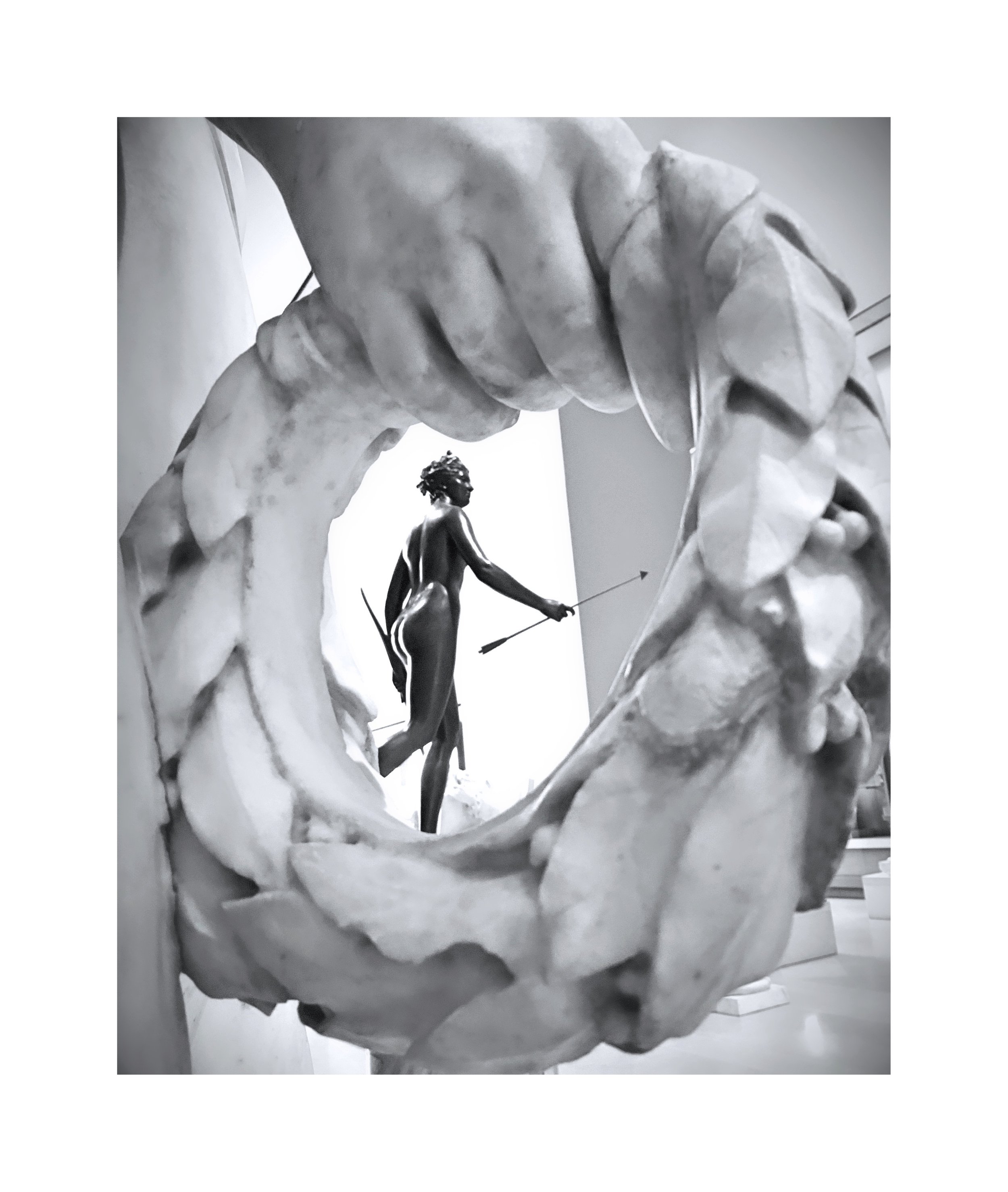 Une sculpture en marbre représentant une figure humaine ou mythologique, photographiée à travers un cadre circulaire sculpté avec des détails intriqués.