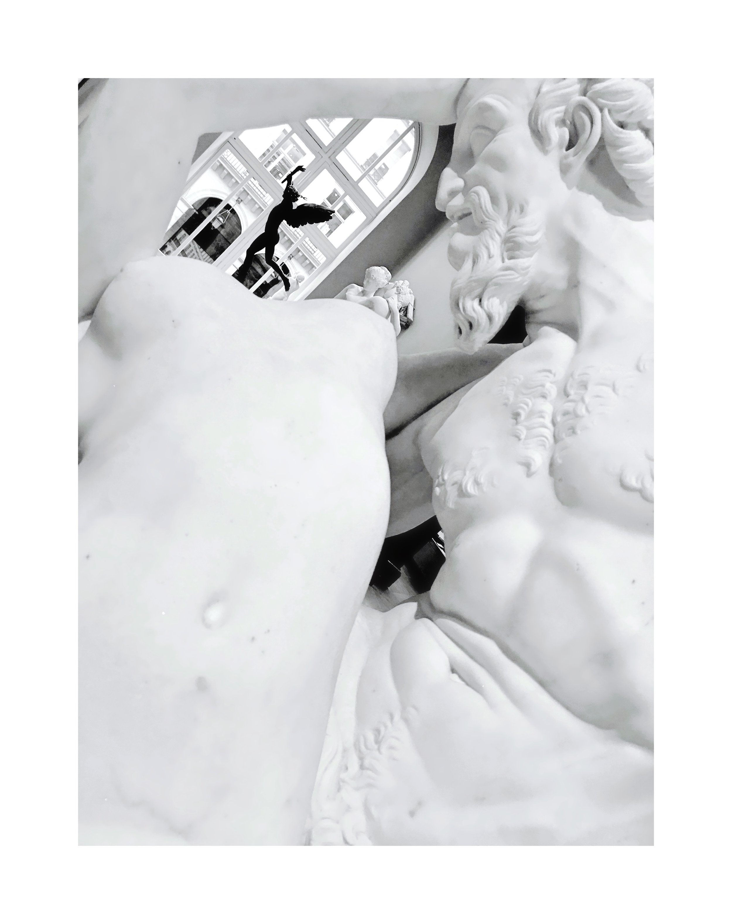 Une sculpture en marbre représentant un homme barbu, vue de près, avec des détails fins. À l'arrière-plan, une figure en silhouette noire, probablement une décoration ou une sculpture, se détache contre une fenêtre avec des carreaux.