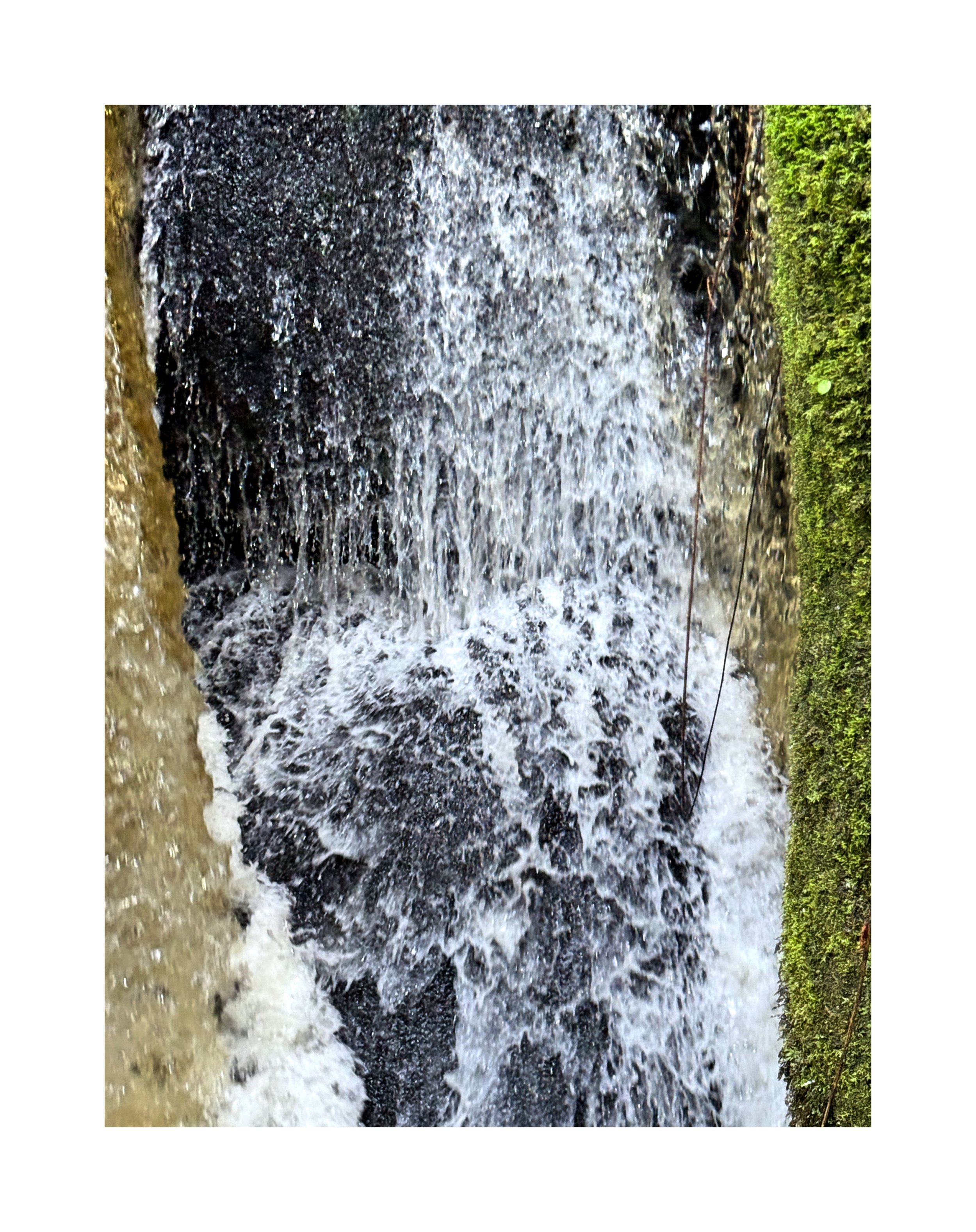 Une cascade d'eau qui déferle sur des rochers, entourée de mousse verte.