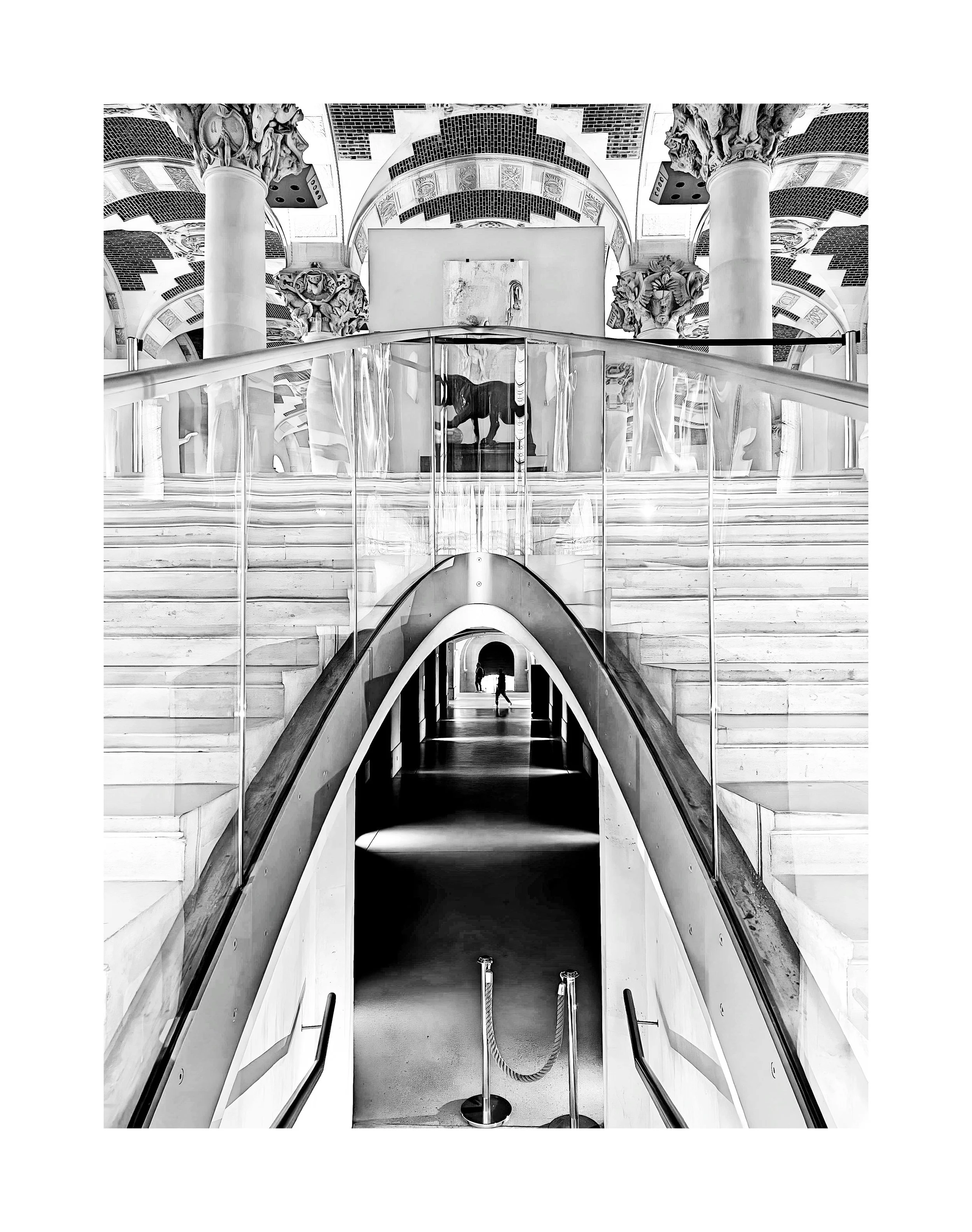Une image en noir et blanc d’un intérieur d’un bâtiment avec des escaliers, un escalator, des colonnes ornées et une œuvre d’art ou sculpture en arrière-plan.