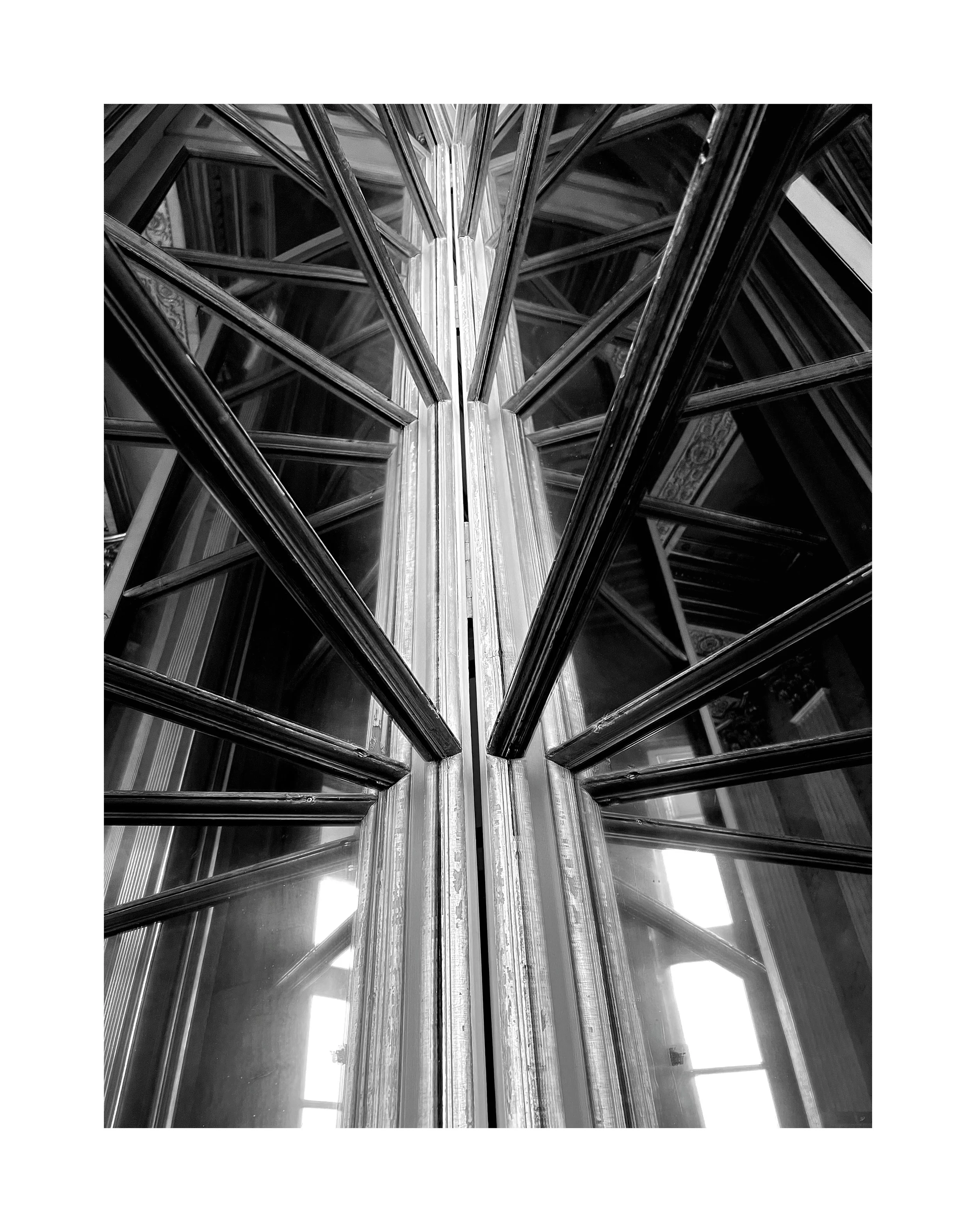 Vue en plongée d'une structure en métal et verre, probablement une fenêtre ou un miroir, avec des lignes géométriques convergentes vers le centre