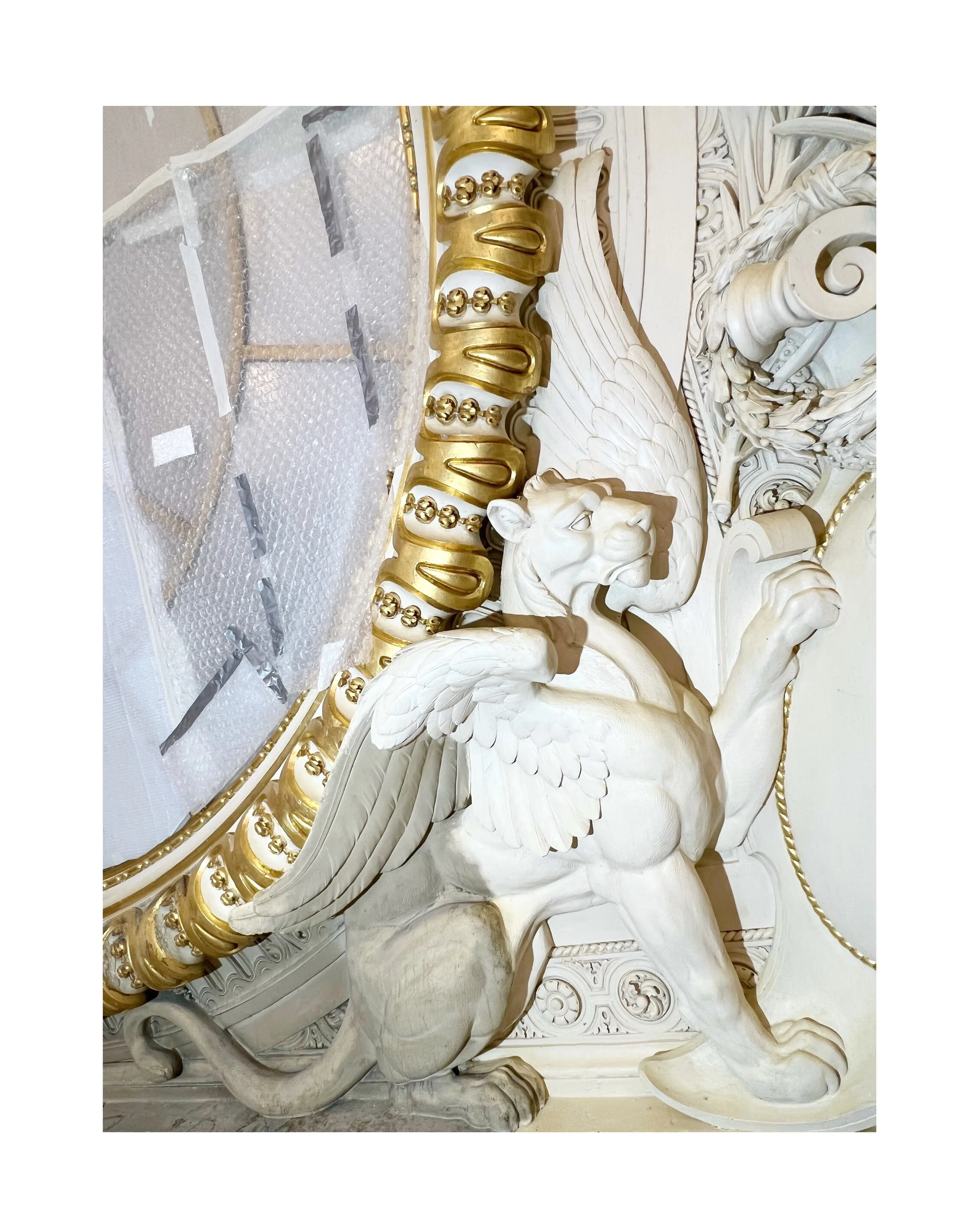 Une sculpture en pierre représentant un lion ailé avec des éléments décoratifs dorés et blancs, partie d'un mobilier orné de détails artistiques.