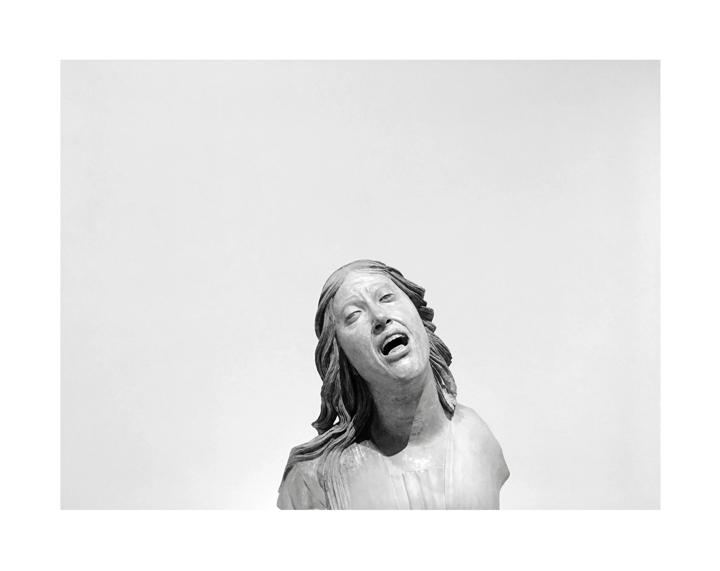 Statue en marbre représentant une femme avec une expression de douleur ou de tristesse, avec des cheveux longs et ondulés, sur un fond blanc