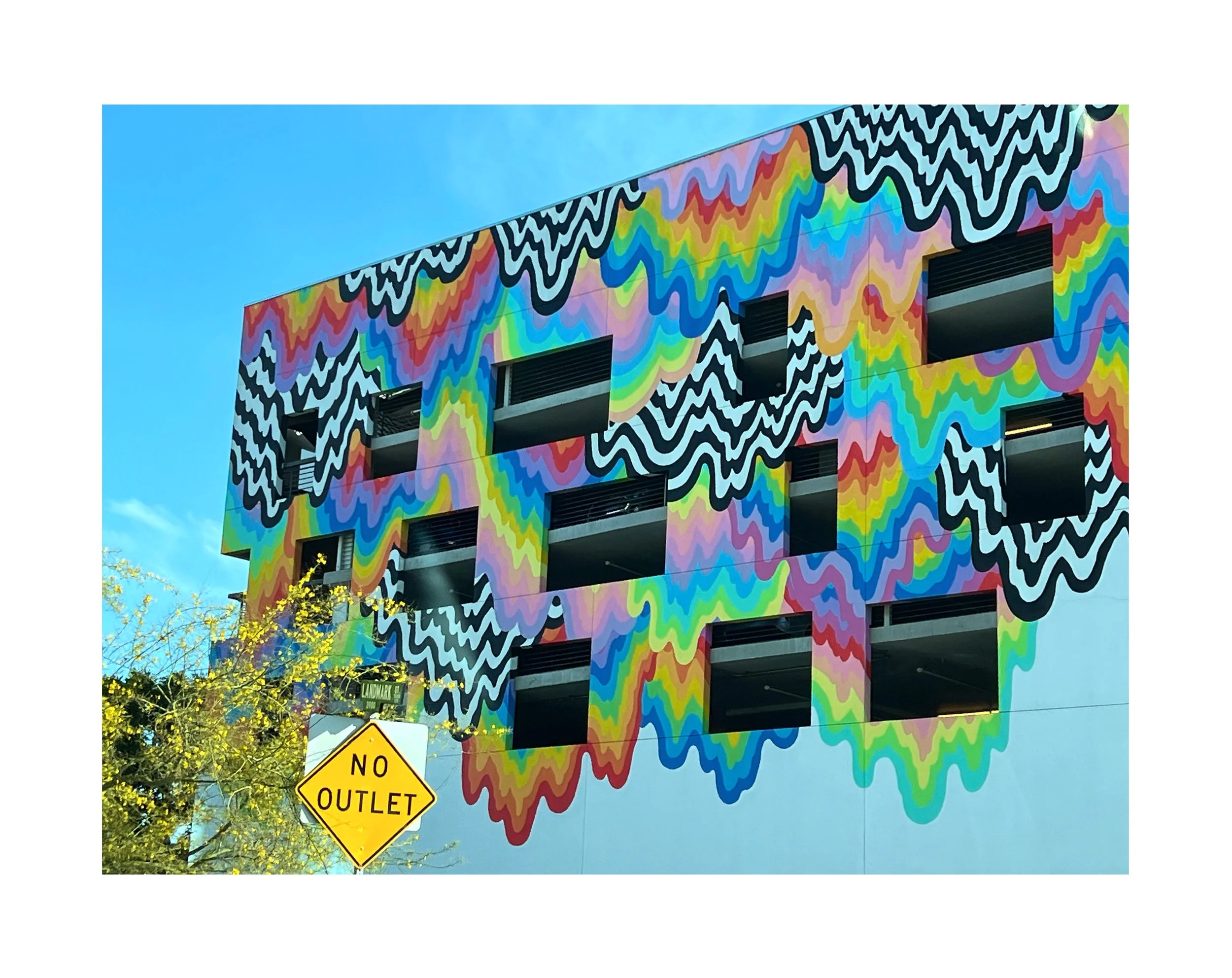 Façade d'un bâtiment avec une peinture murale colorée et abstraite. On voit un panneau jaune 'No Outlet' en bas à gauche.