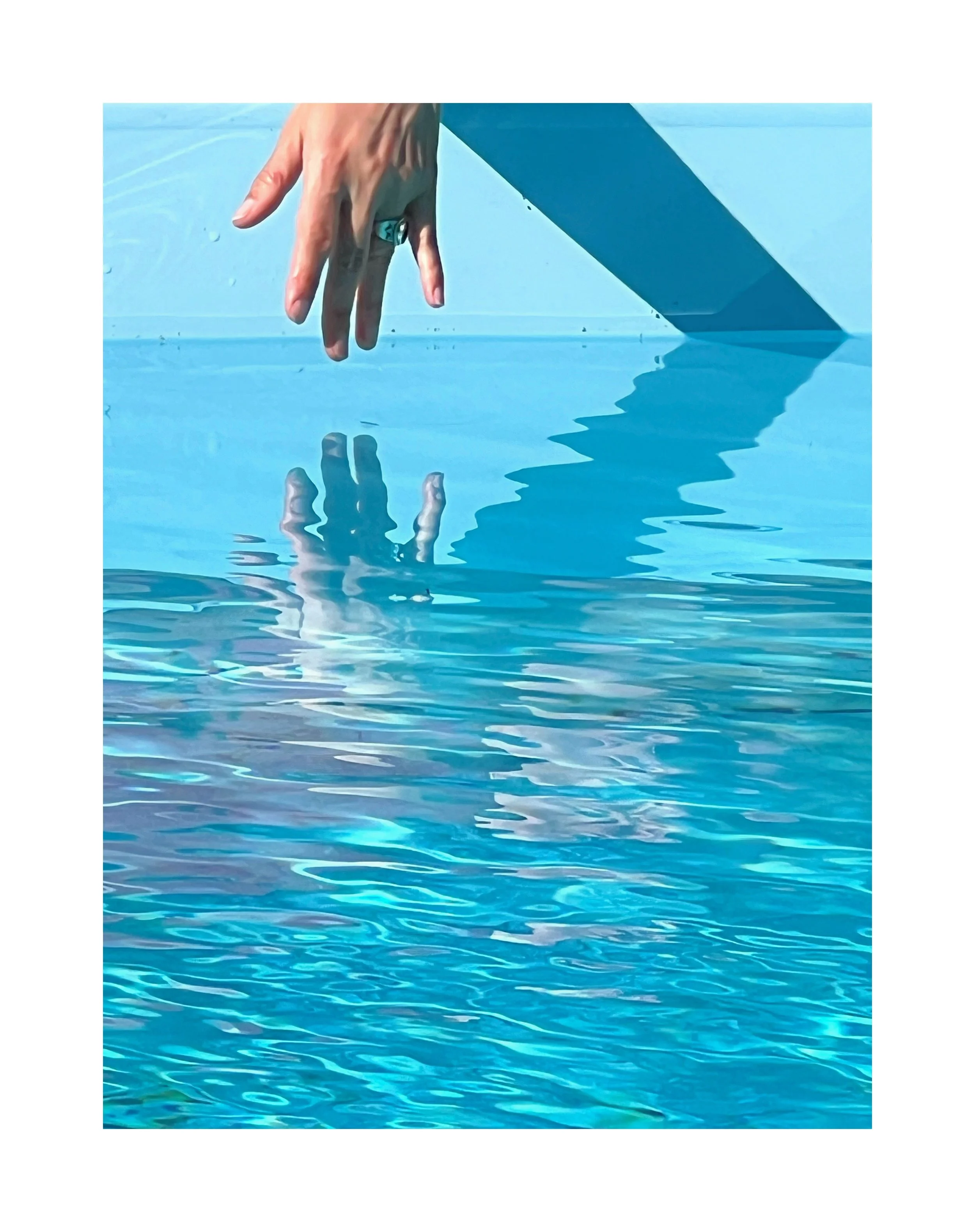 Une main qui touche la surface d'une piscine bleue, créant une réflexion dans l'eau.