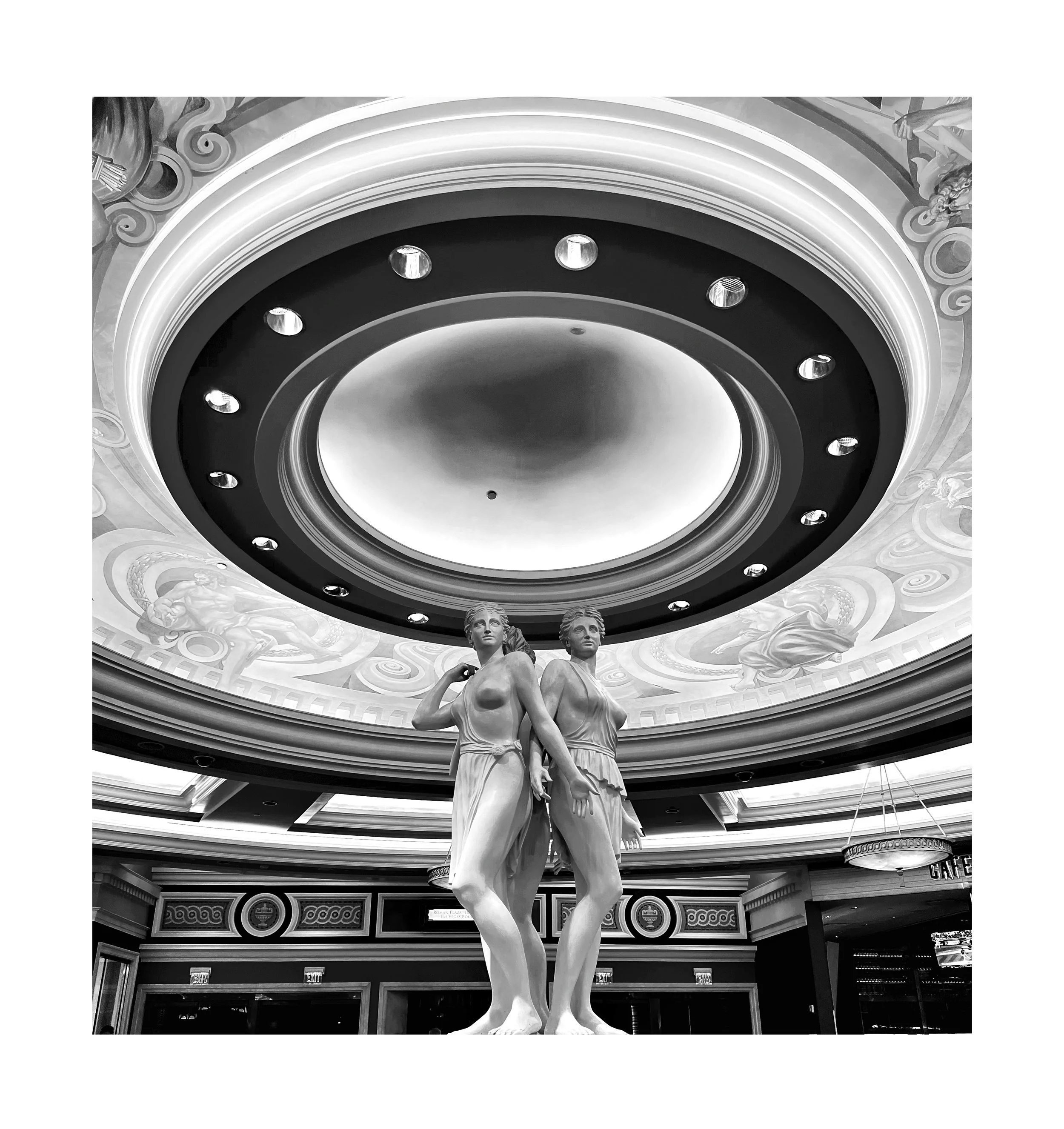 Deux statues de femmes en marbre dans un intérieur élégant, avec un plafond orné de fresques et un grand luminaire circulaire