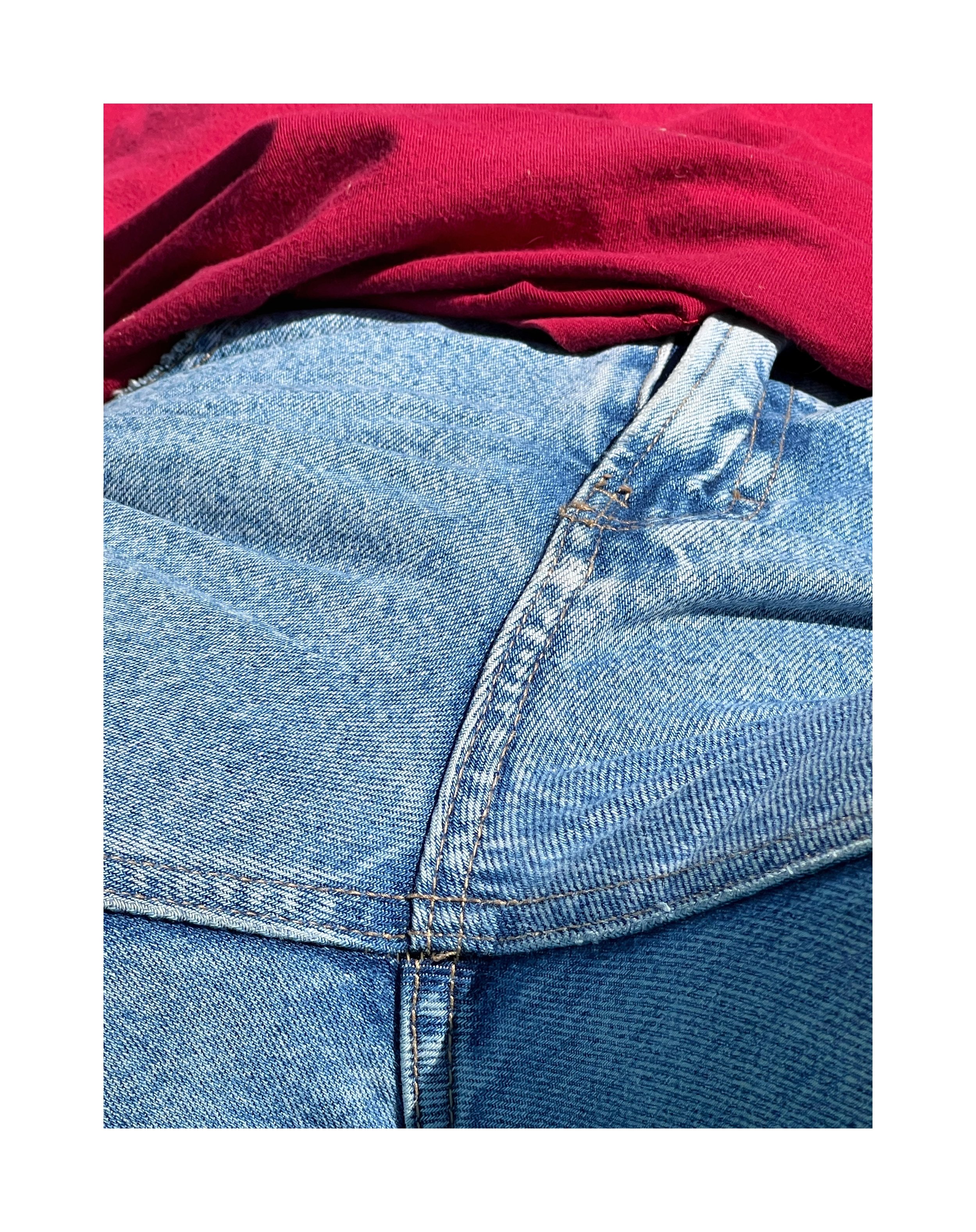 Détail d'un jean bleu avec une couture visible, porté sous un haut rouge.