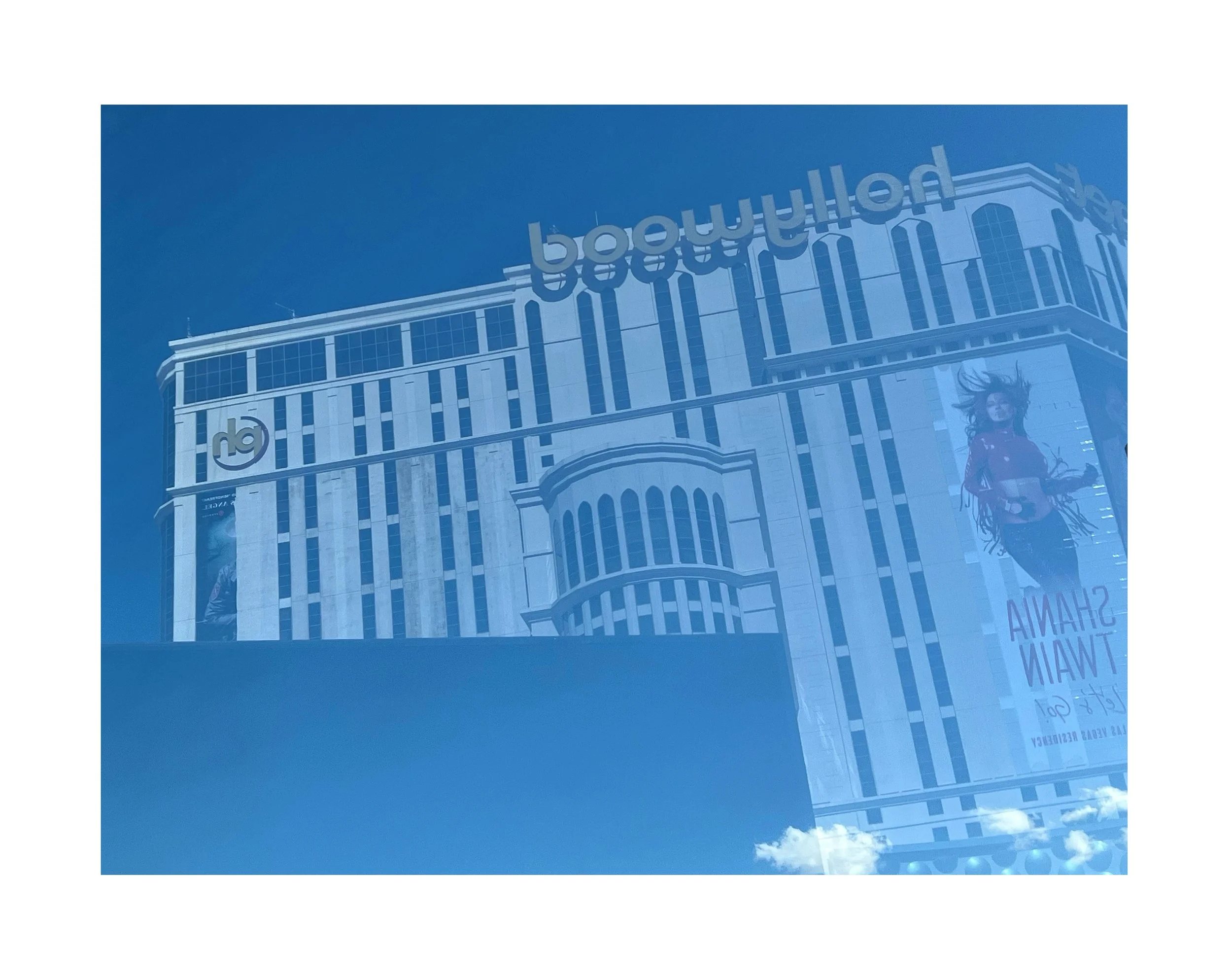 Reflet d'un bâtiment moderne avec des affiches publicitaires sur la façade, sous un ciel bleu.