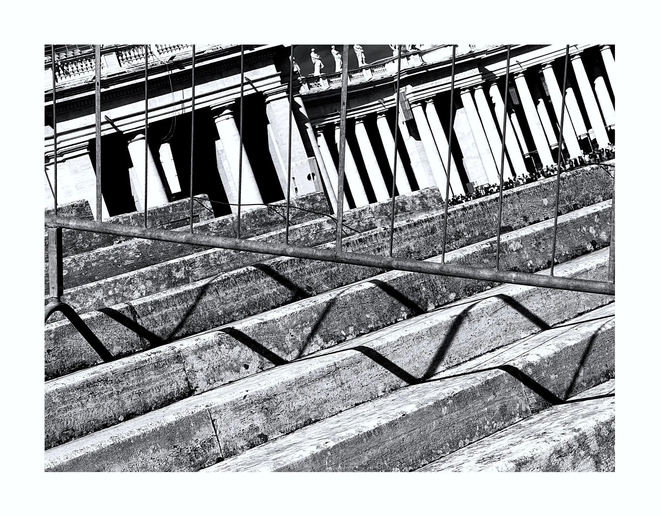 Escaliers en pierre avec des barrière en métal et un bâtiment avec des colonnes en arrière-plan, en noir et blanc.