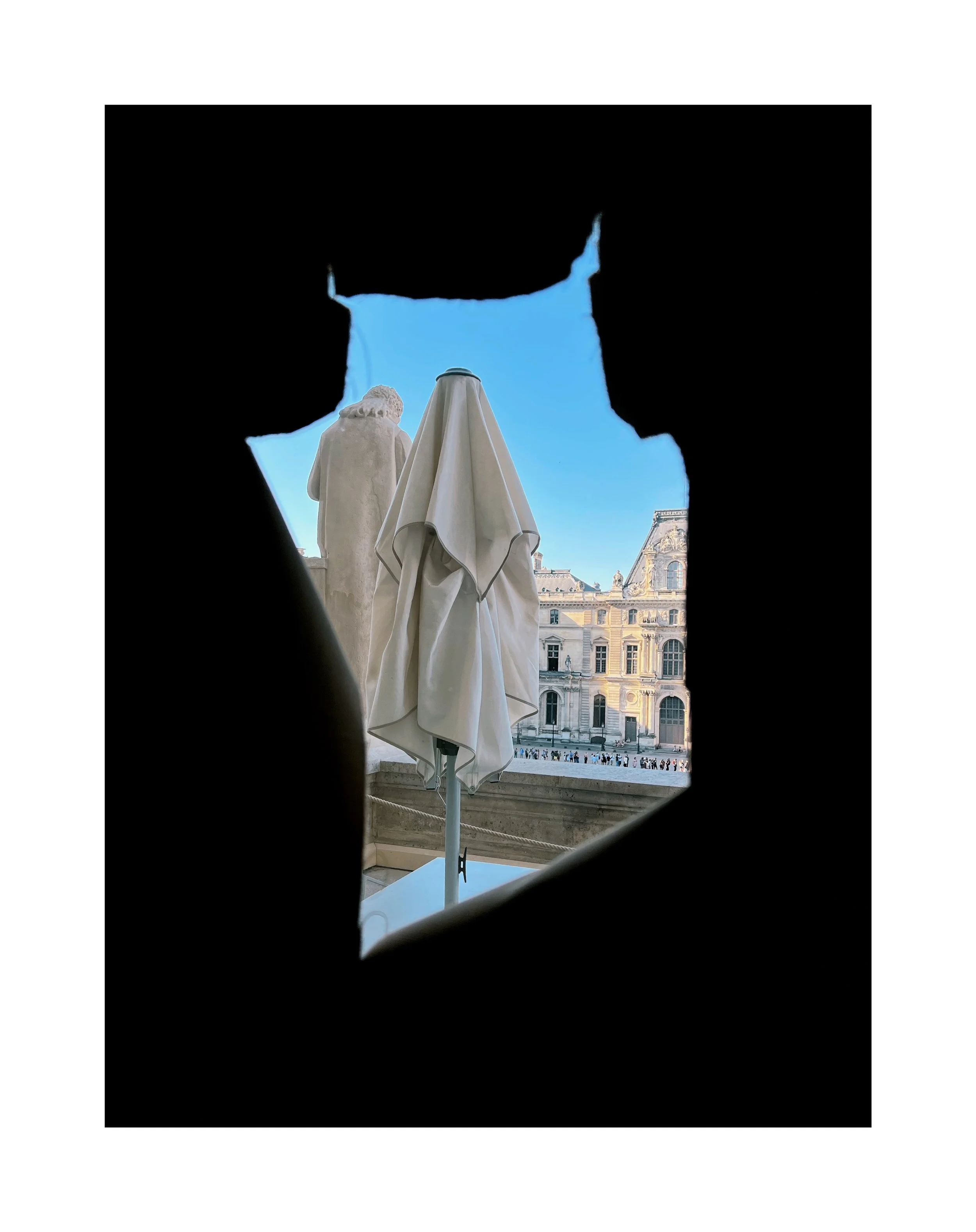 Vue d'une place historique à travers une ouverture dans une structure noire, montrant une statue, un parasol blanc fermé, et un bâtiment antique en arrière-plan.