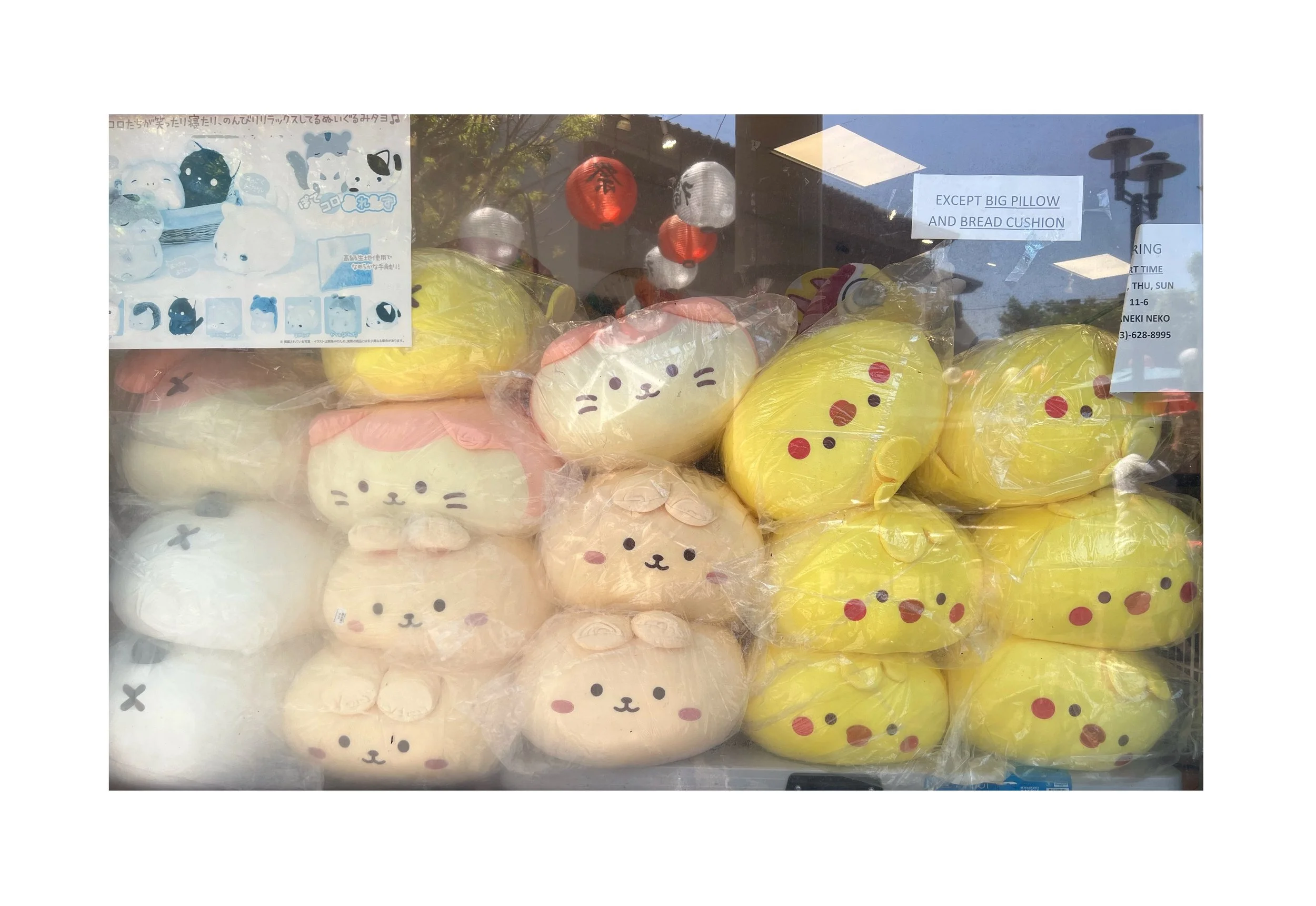Peluches en forme de personnages mignons et jaunes dans une vitrine de magasin, avec quelques pancartes et lumières reflétées à l'extérieur.