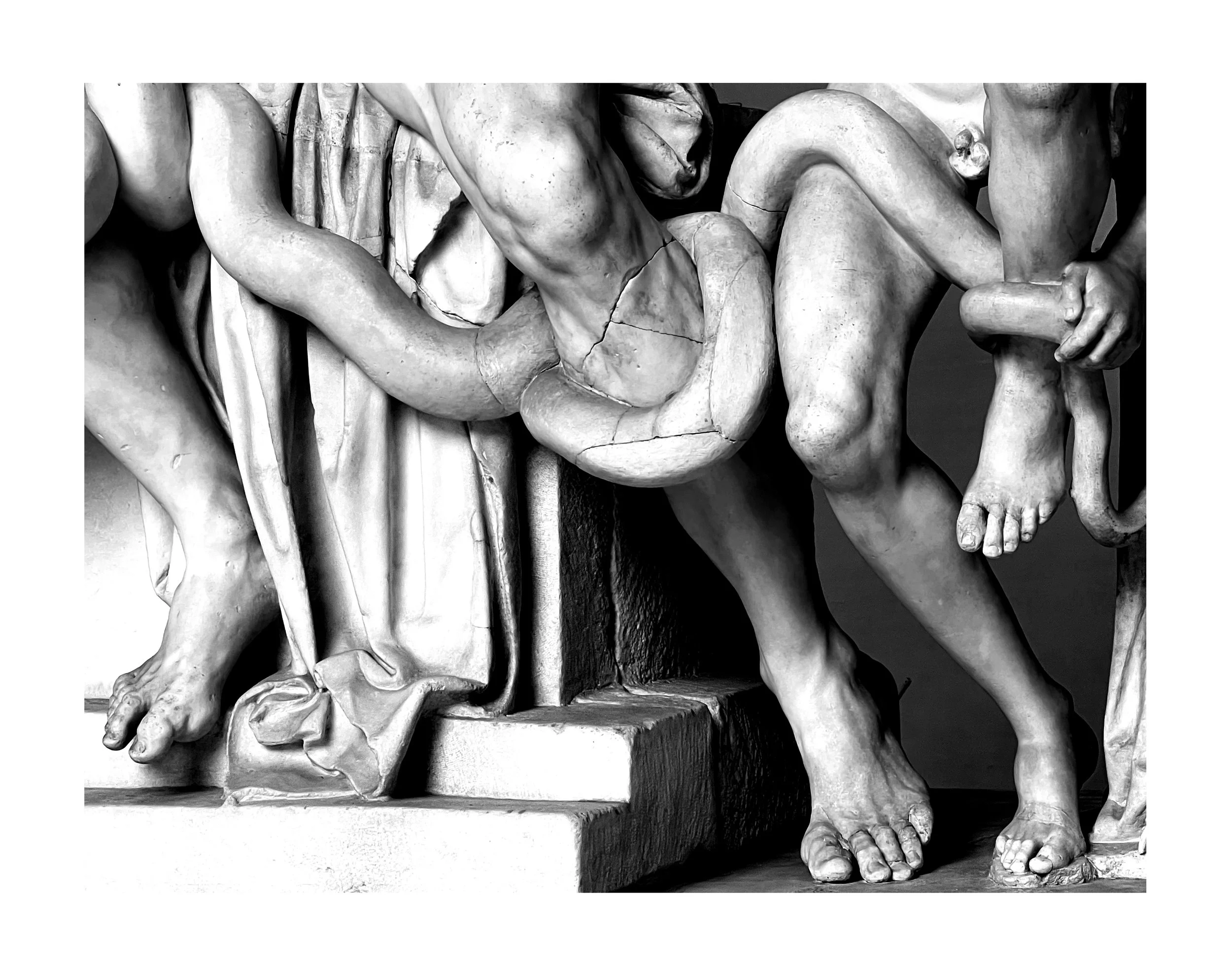 Détail d'une sculpture en marbre noir et blanc représentant des figures humaines attachées ou enchaînées, mettant en évidence des bras, jambes et parties de corps.