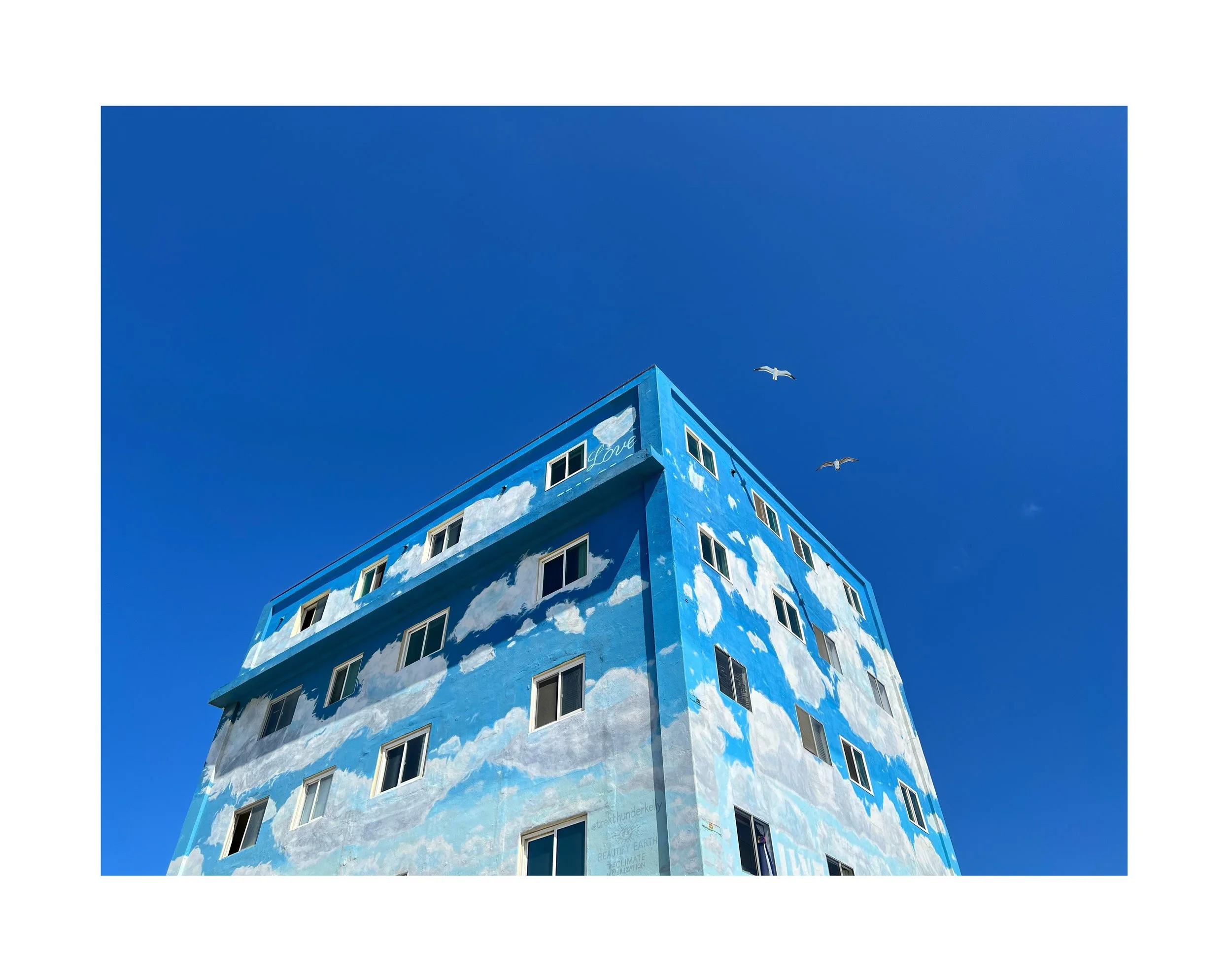 Immeuble peint avec un motif de ciel bleu et de nuages, avec deux oiseaux volant dans le ciel.