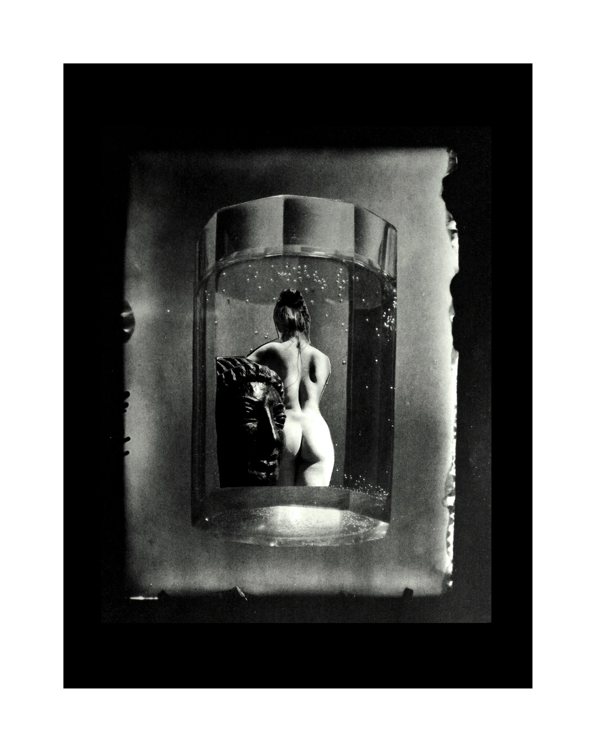 Une femme nue vue de dos dans un bain à remous en verre avec une tête de sculpture à côté dans une pièce sombre.