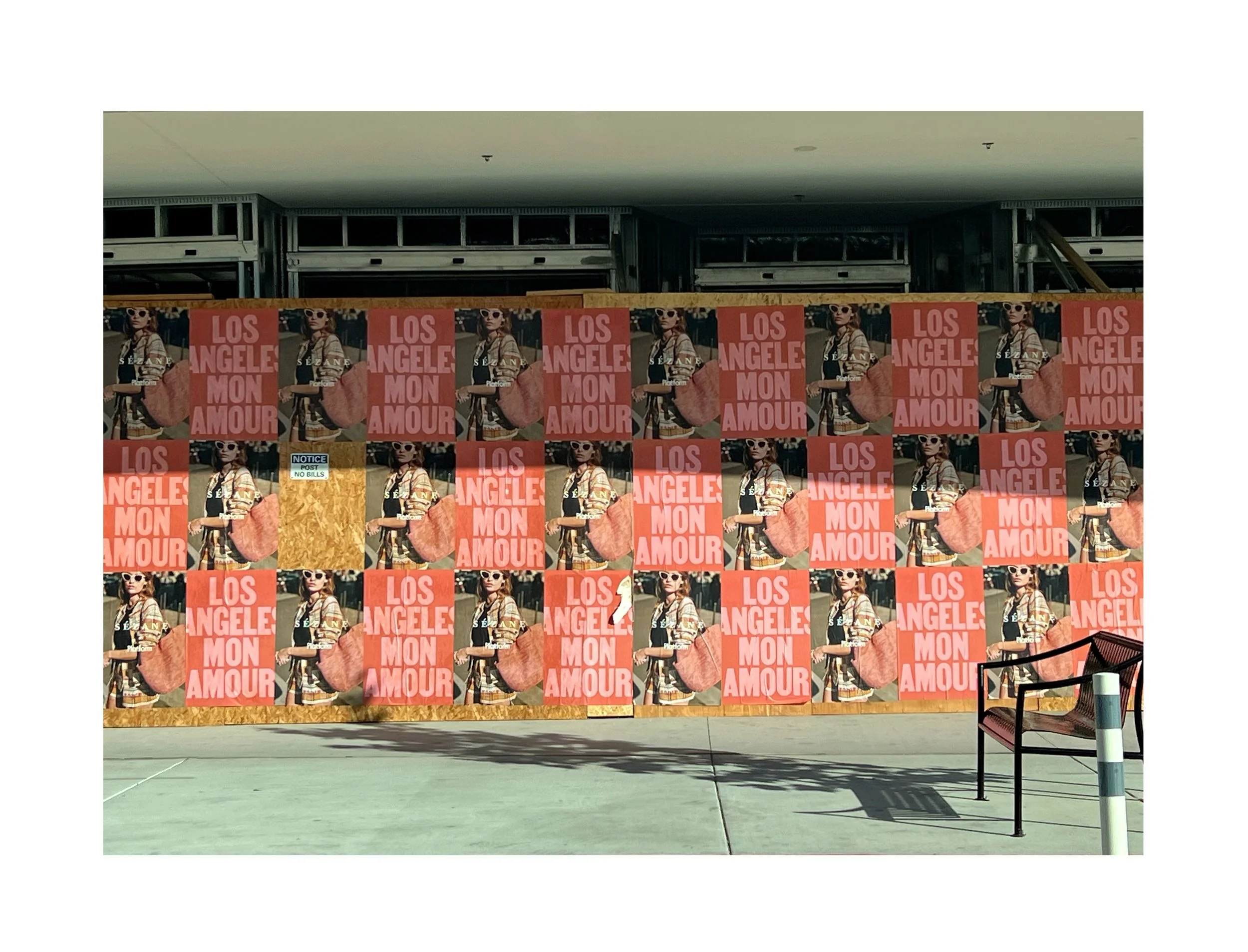Un mur d'affiches roses avec une photo d'une femme portant des lunettes de soleil, une veste à rayures, et un sac de plage, accompagnée du texte "Los Angeles Mon Amour".