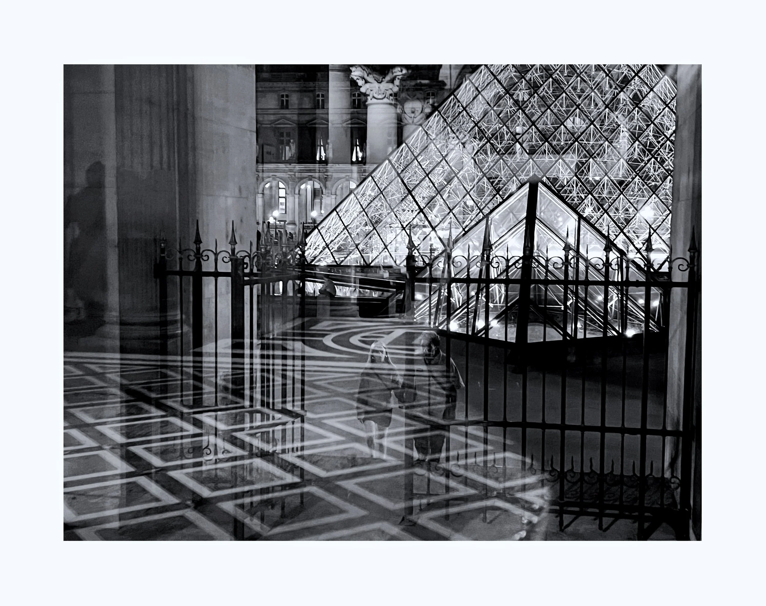 Une scène nocturne à l'intérieur du musée du Louvre, montrant la pyramide en verre illuminée, une grille noire en avant-plan, et deux personnes assises au sol.