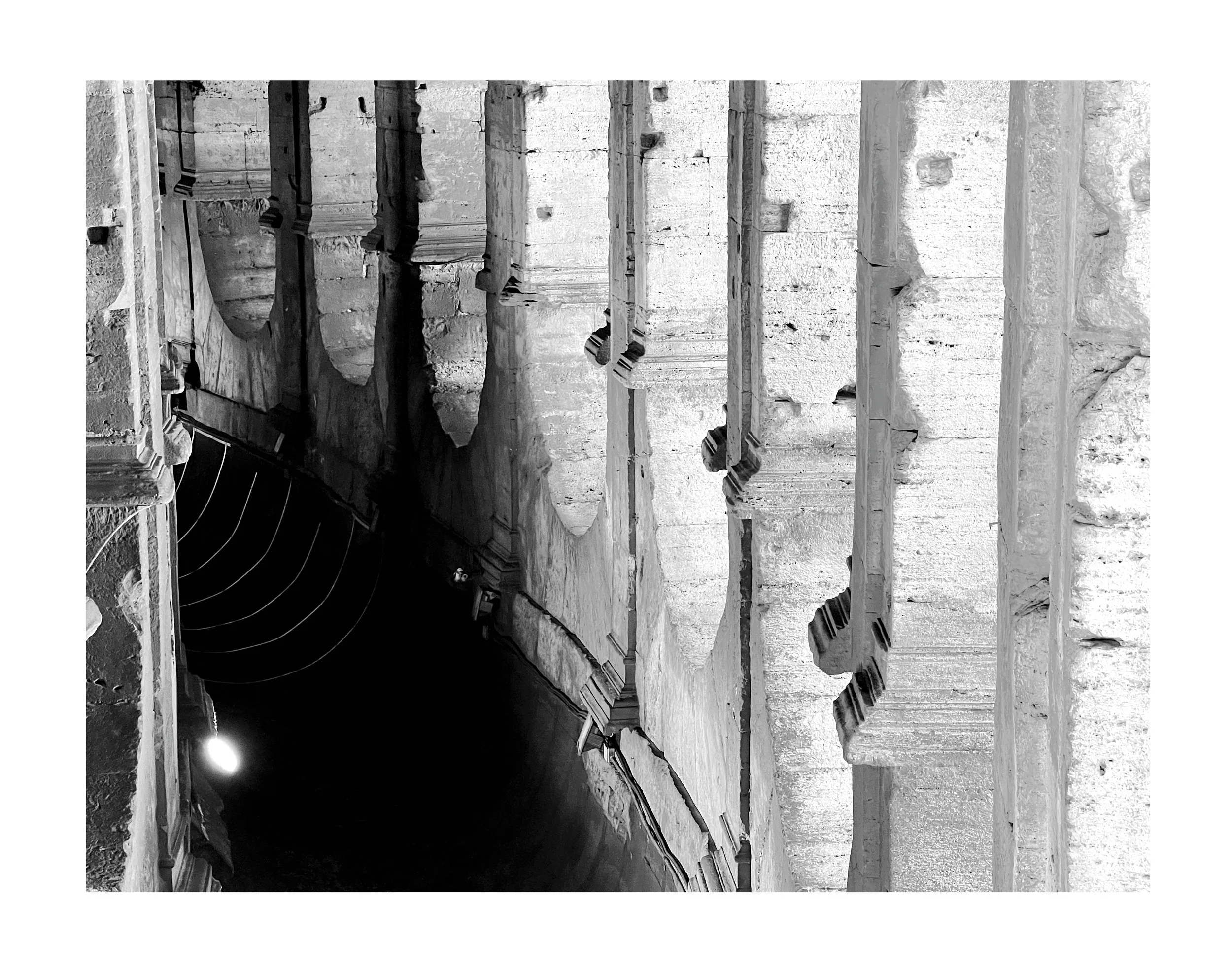 Vestiges d'une ancienne structure en pierre, avec des colonnes effondrées et des escaliers en ruine, photographie en noir et blanc.