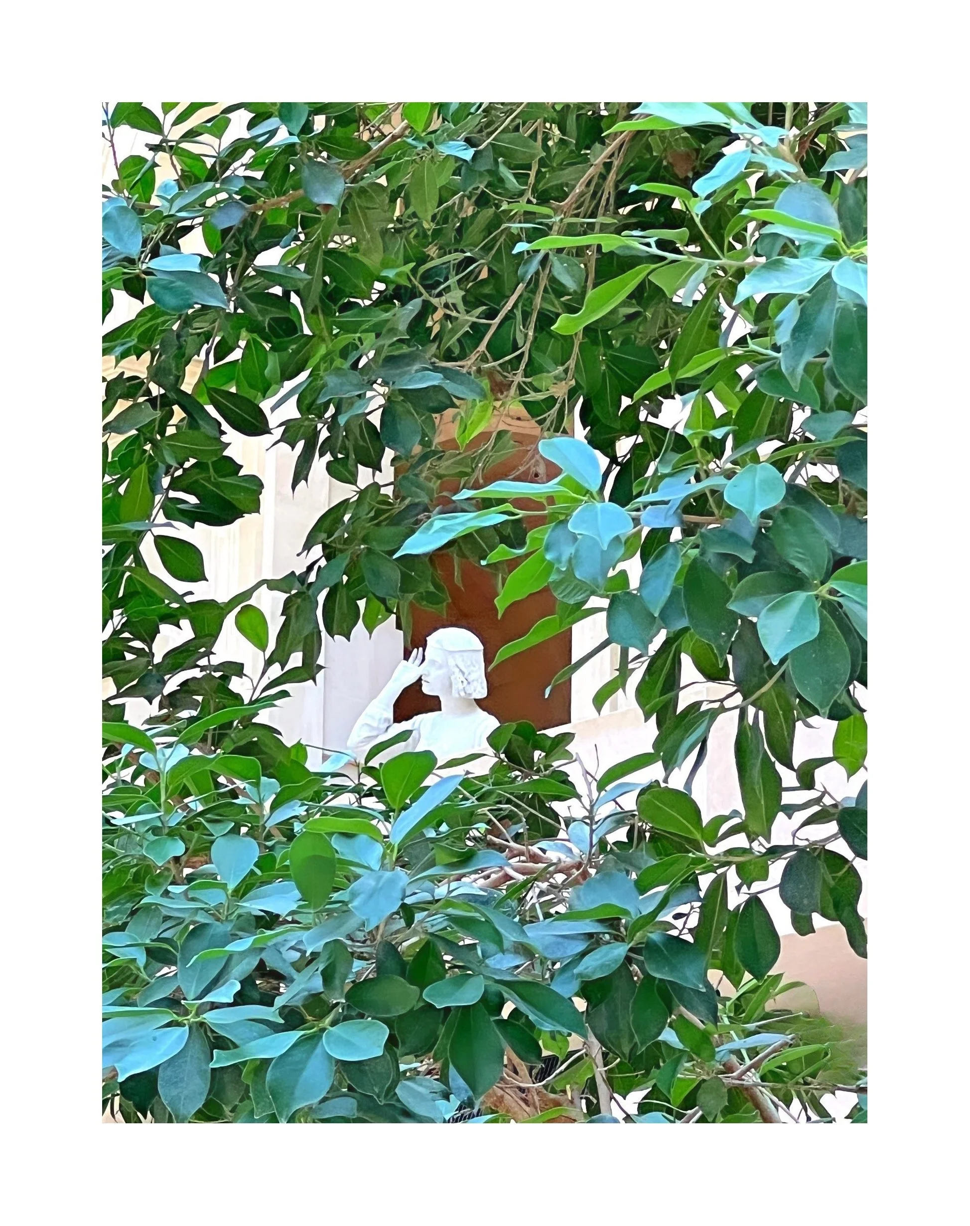 Statue de petite fille en train de faire un salut de la main, partiellement dissimulée par la végétation verte dense.