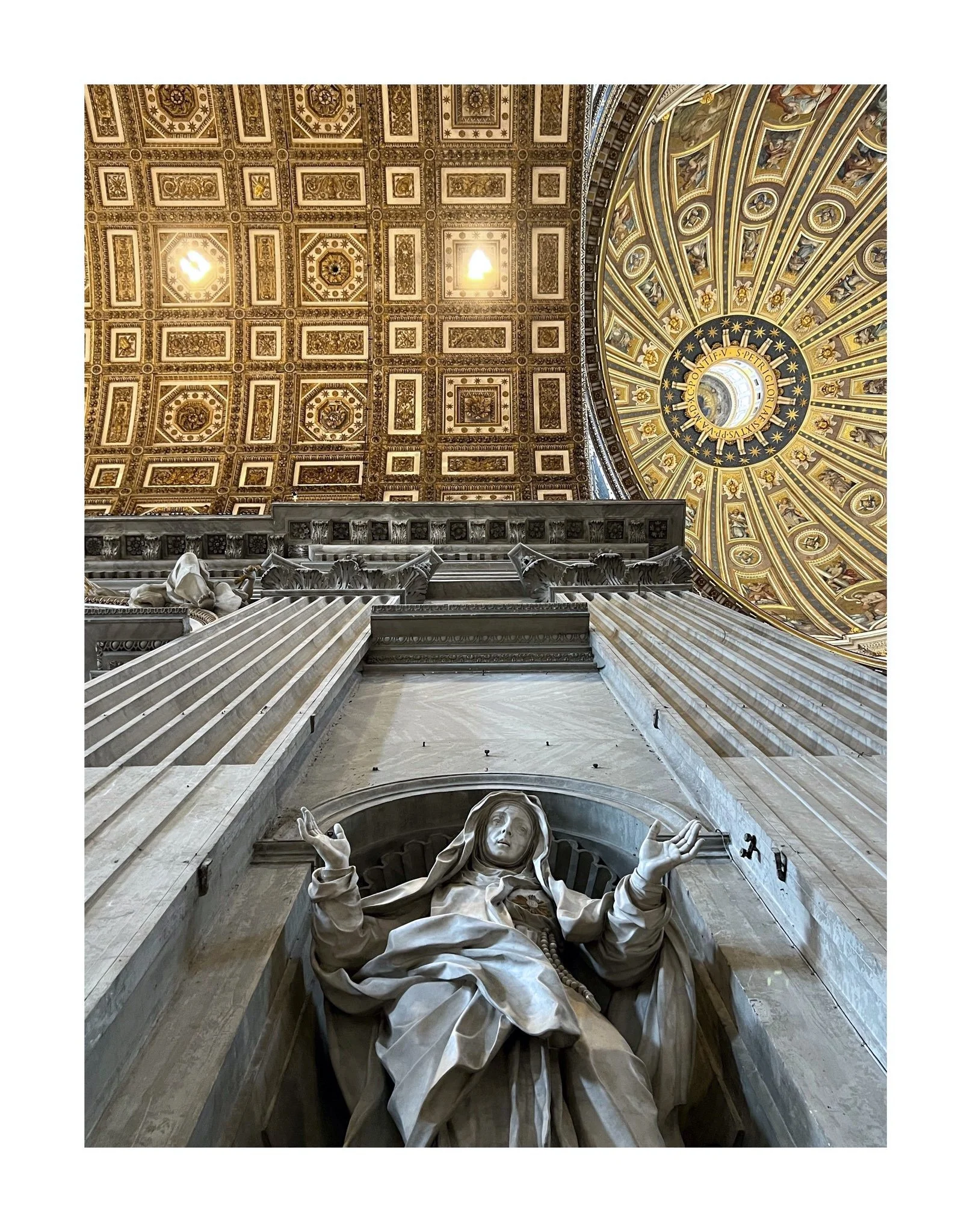 Vue intérieure d'une basilique avec une statue religieuse en premier plan, de haut plafond décoré de fresques et d'or, et un dôme avec un zodiaque au centre.