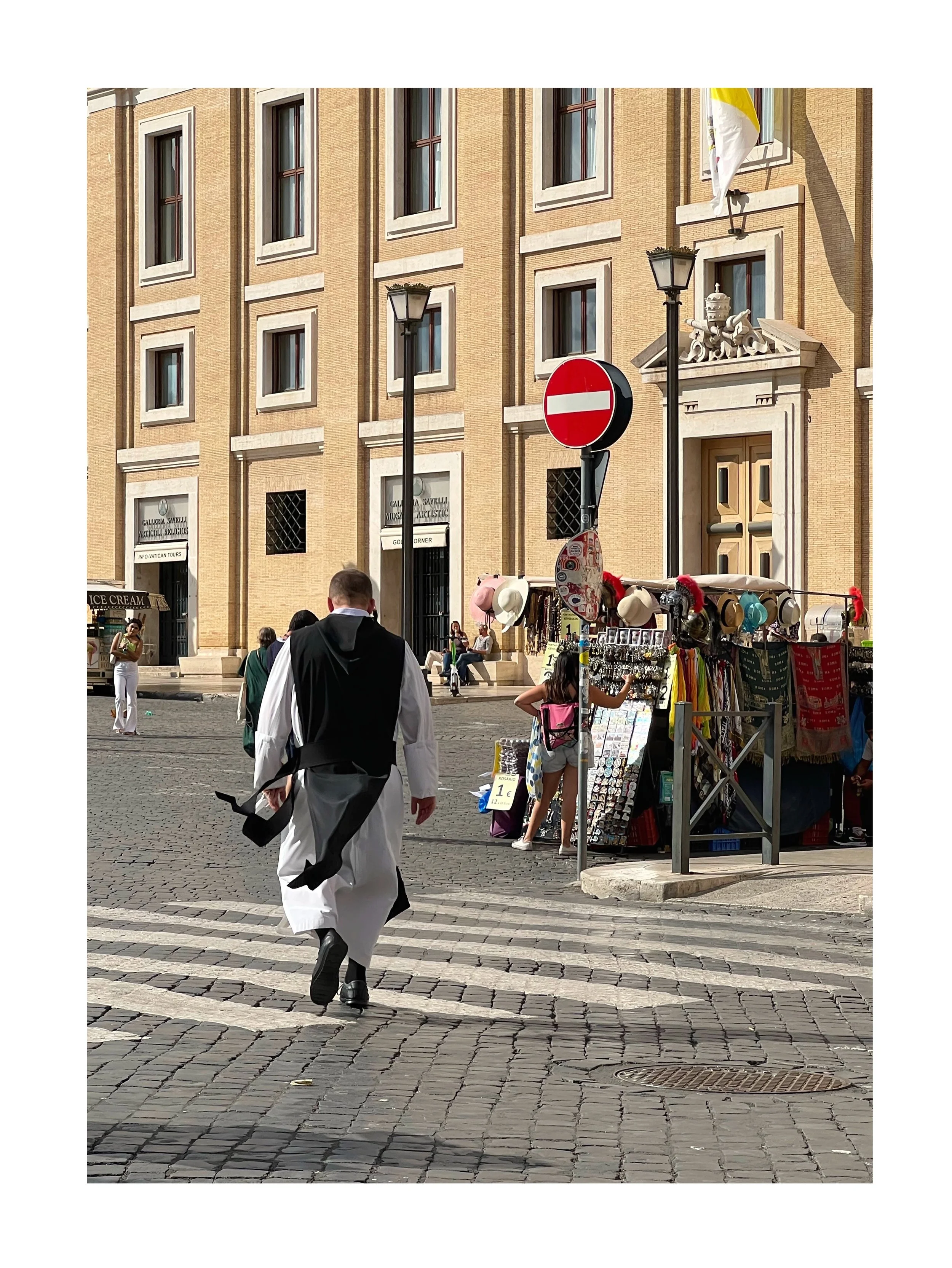 Un homme en costume traditionnel marchant dans une rue pavée, avec un bâtiment en arrière-plan et un étalage de souvenirs à côté.