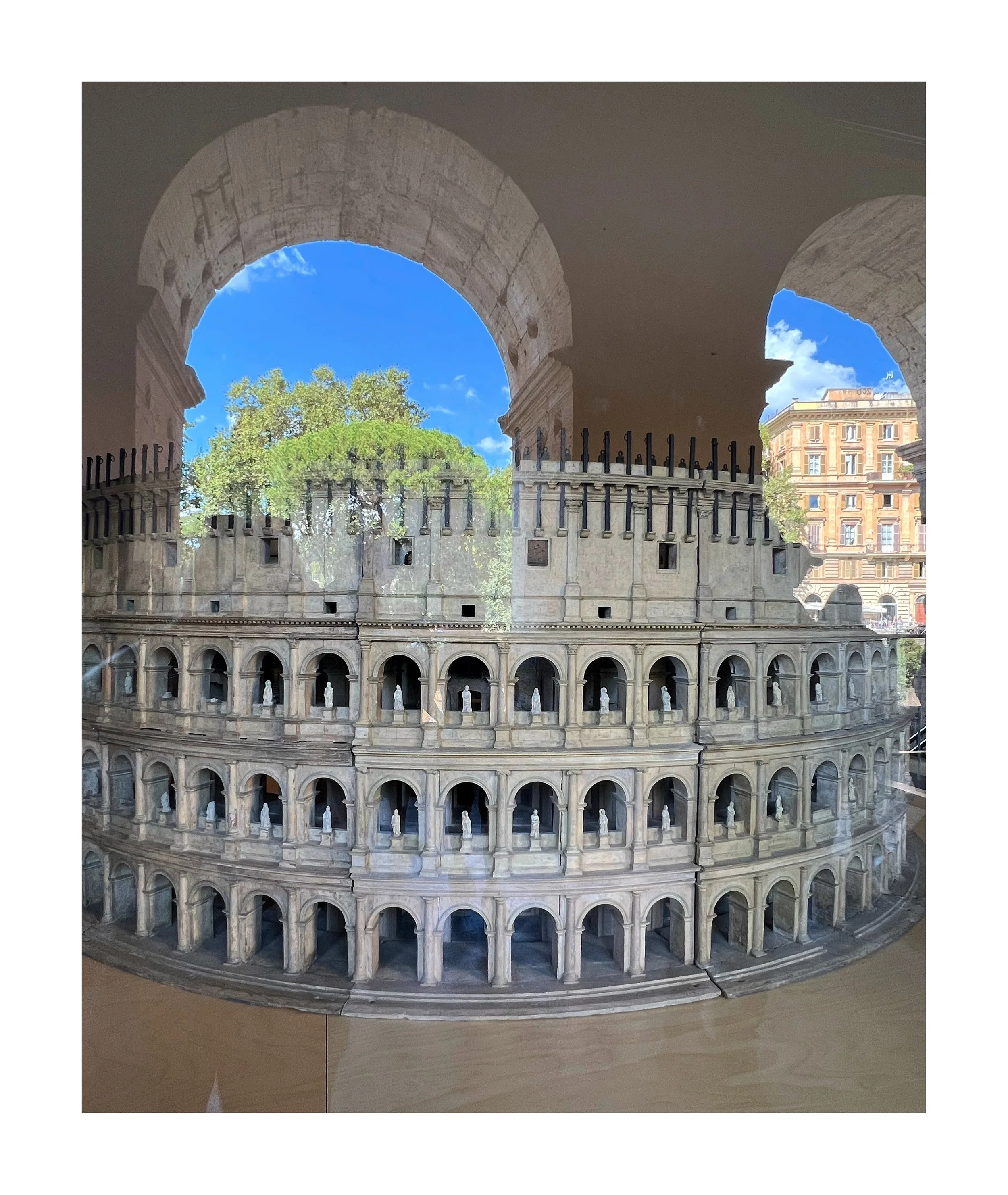 Modèle réduit du Colisée visible à travers une fenêtre archivée avec des arbres et bâtiments en arrière-plan, dans un musée ou une exposition.