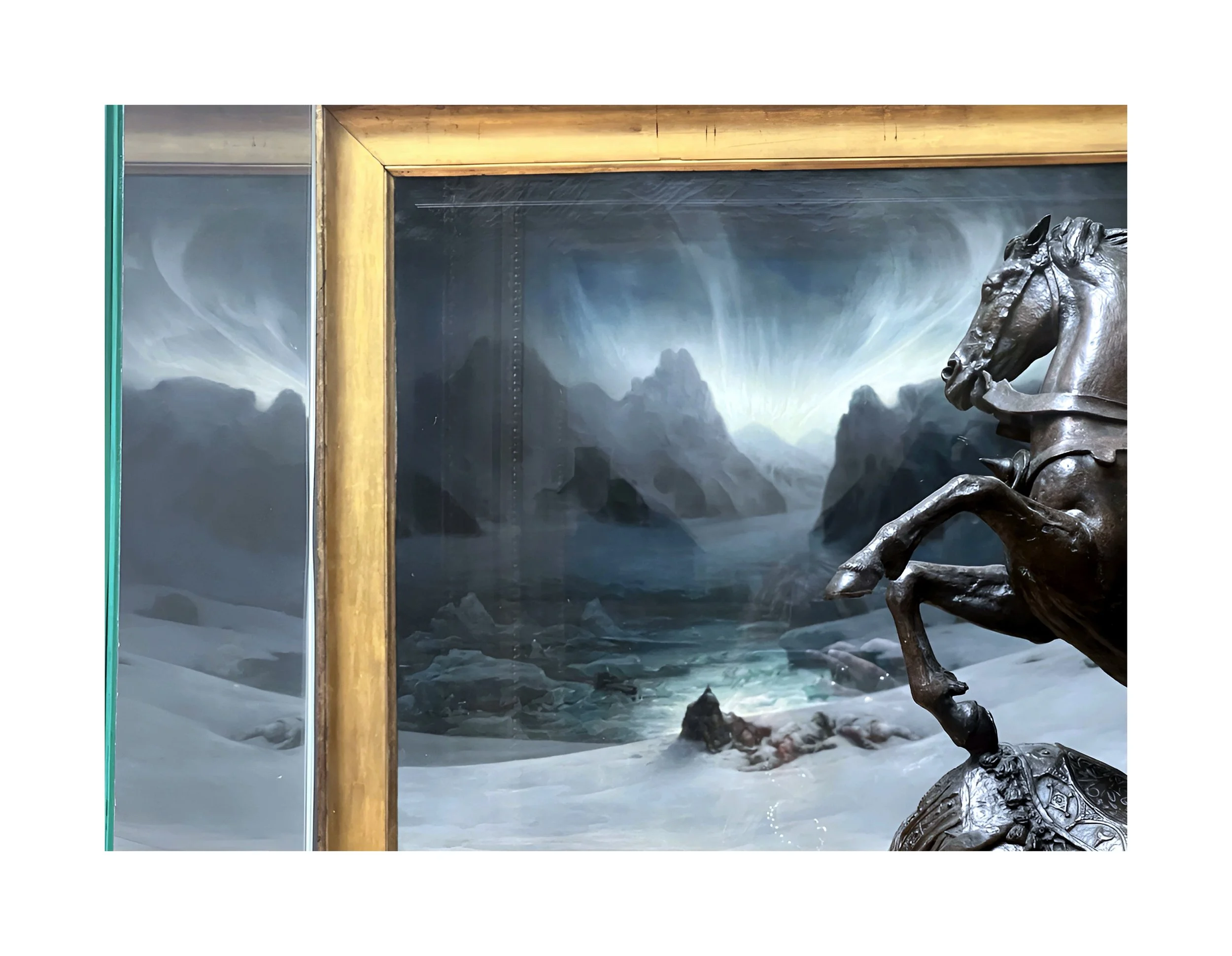 Une sculpture en métal d'un chevalier en armure sur un cheval, avec un paysage de montagnes enneigées et une rivière glacée à l'arrière-plan.