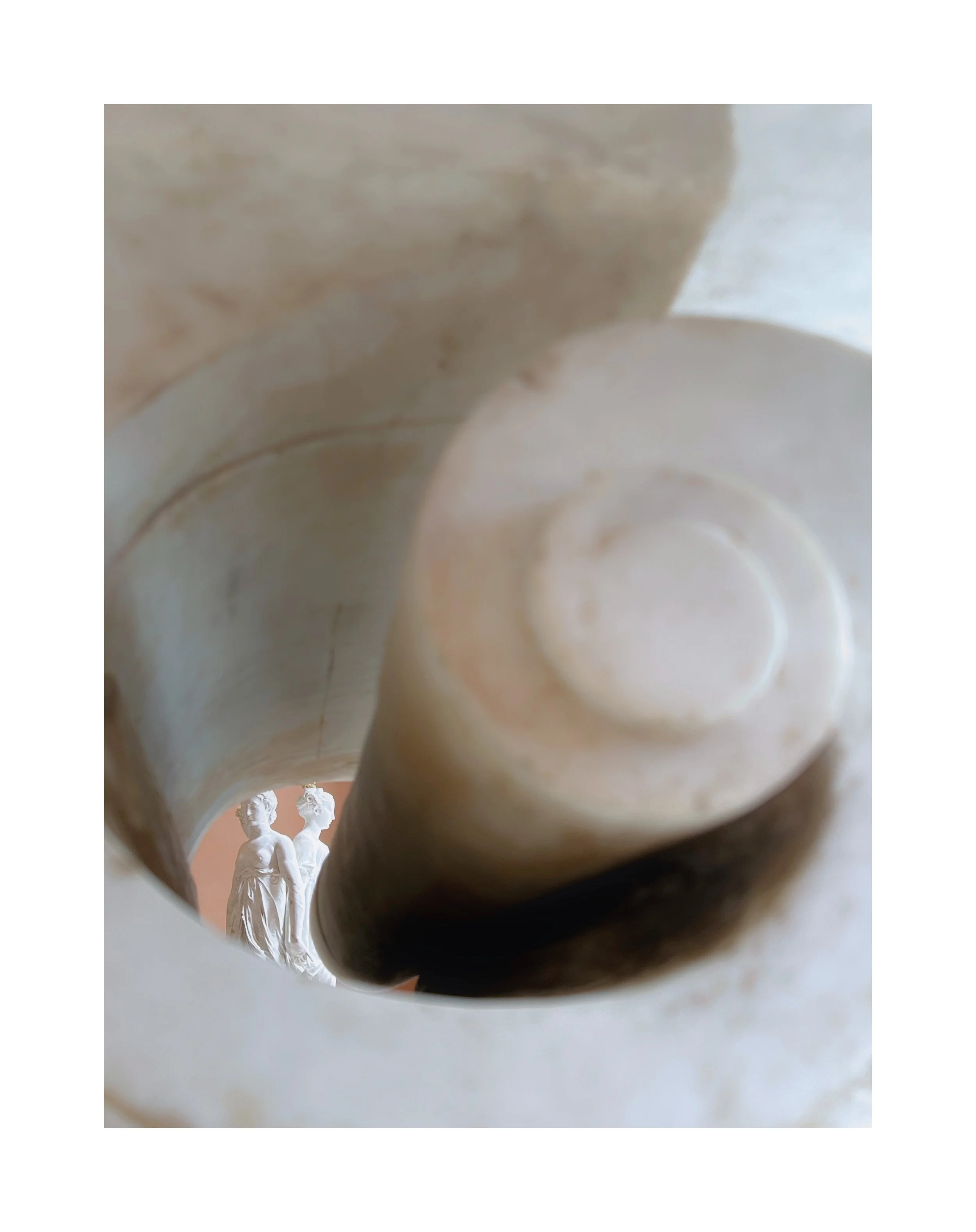 Vue en plongée d'une sculpture en marbre représentant deux figures féminines, vue à travers une ouverture en spirale ou en forme de vortex.