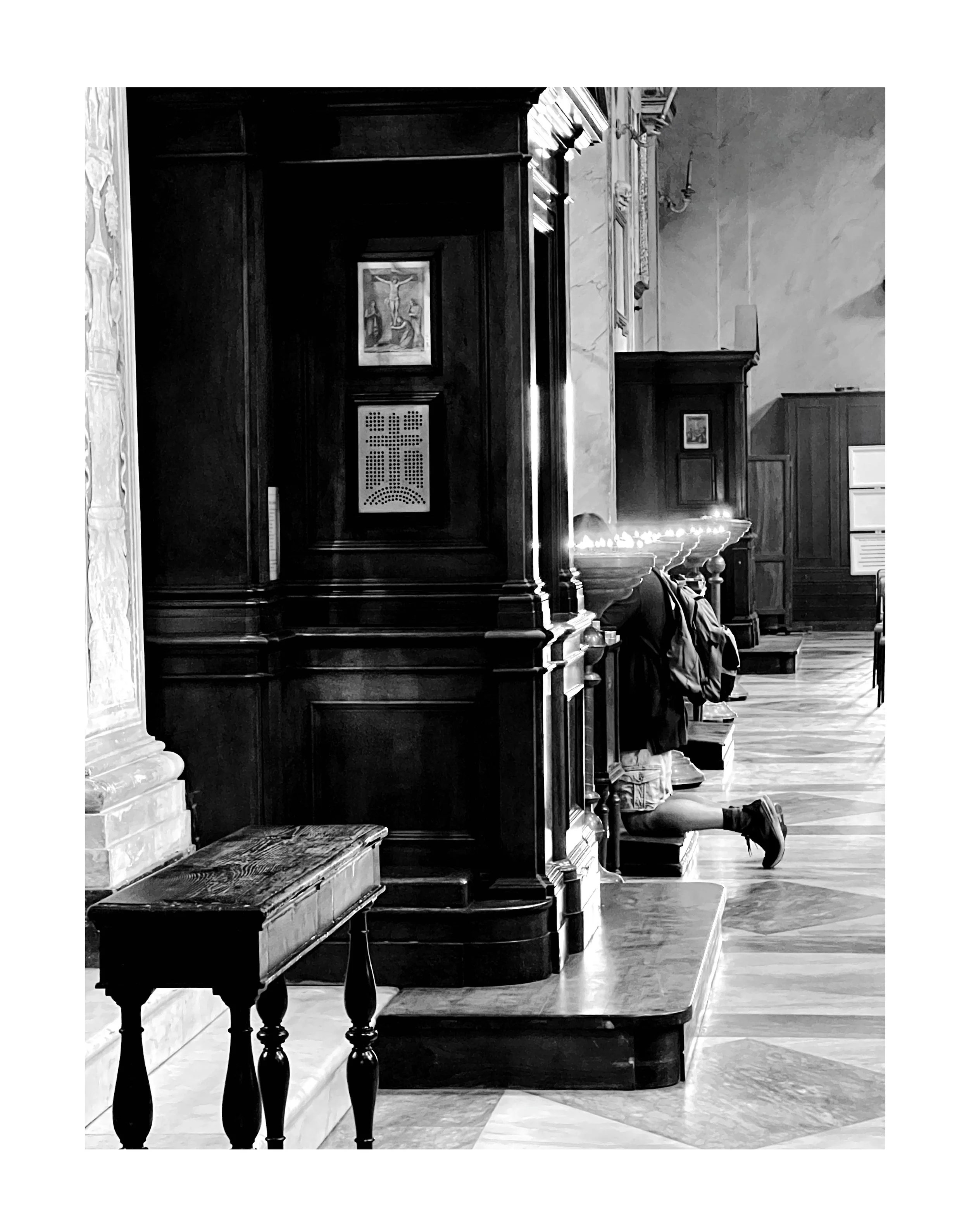 Une personne à genoux dans une église, en prière, avec un cabinet en bois sombre derrière elle.