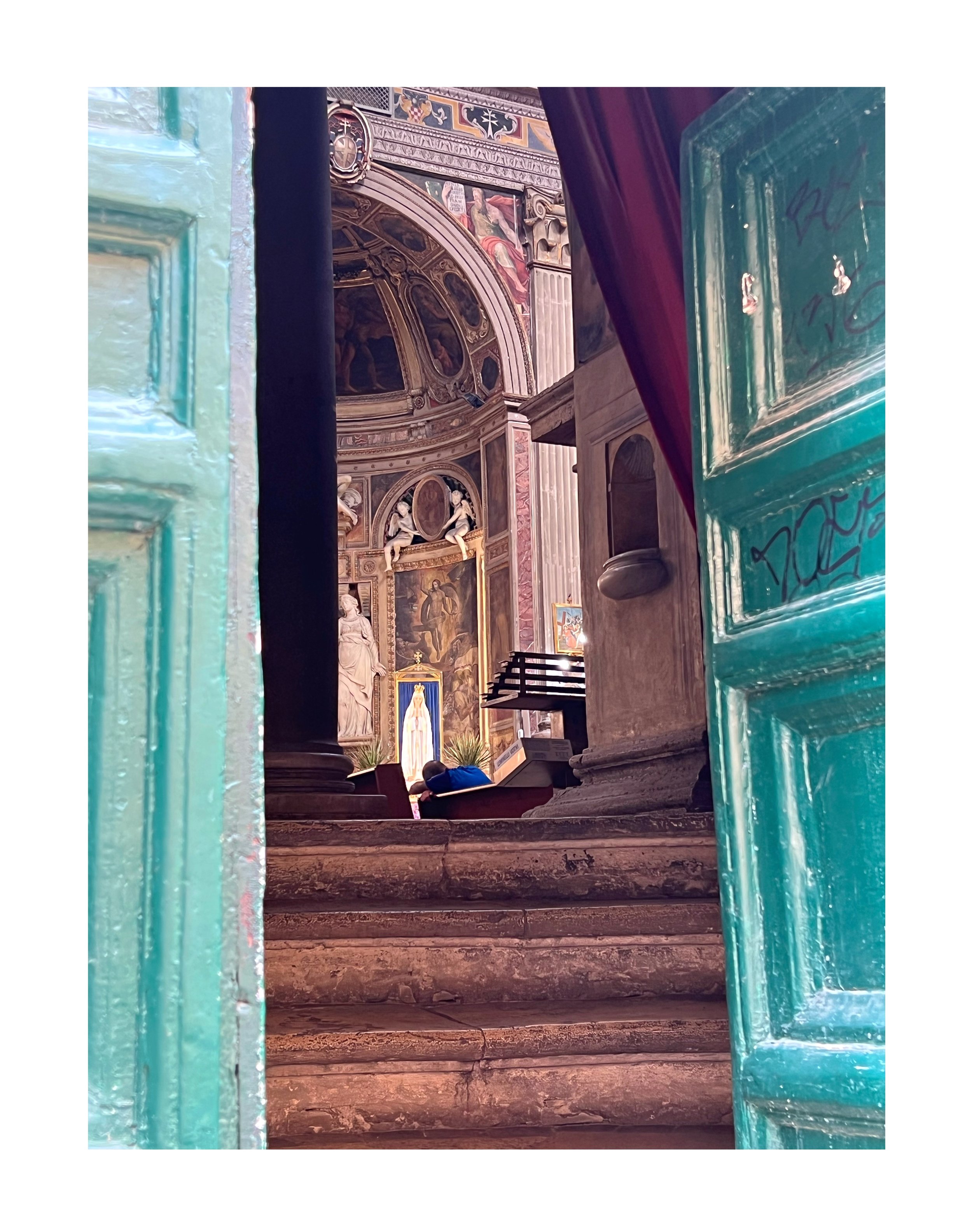 Vue d'une église ou cathédrale avec un intérieur riche en décorations religieuses, à travers une porte en bois peint en vert et une porte de fenêtre. La scène montre des escaliers en pierre menant à un autel ou une fresque religieuse ornée, avec des 