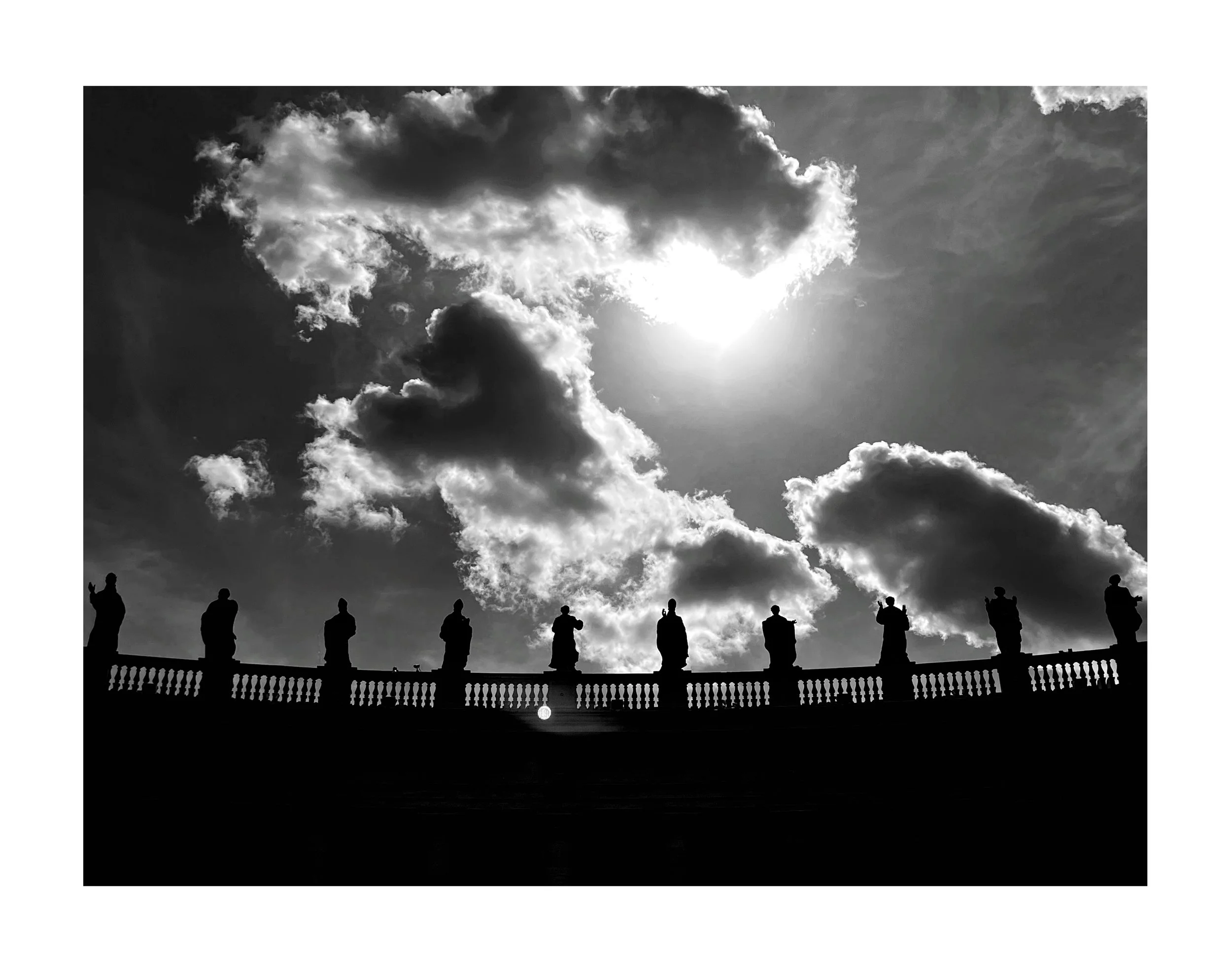 Silhouettes de statues sur un balcon avec un ciel nuageux et ensoleillé en arrière-plan.