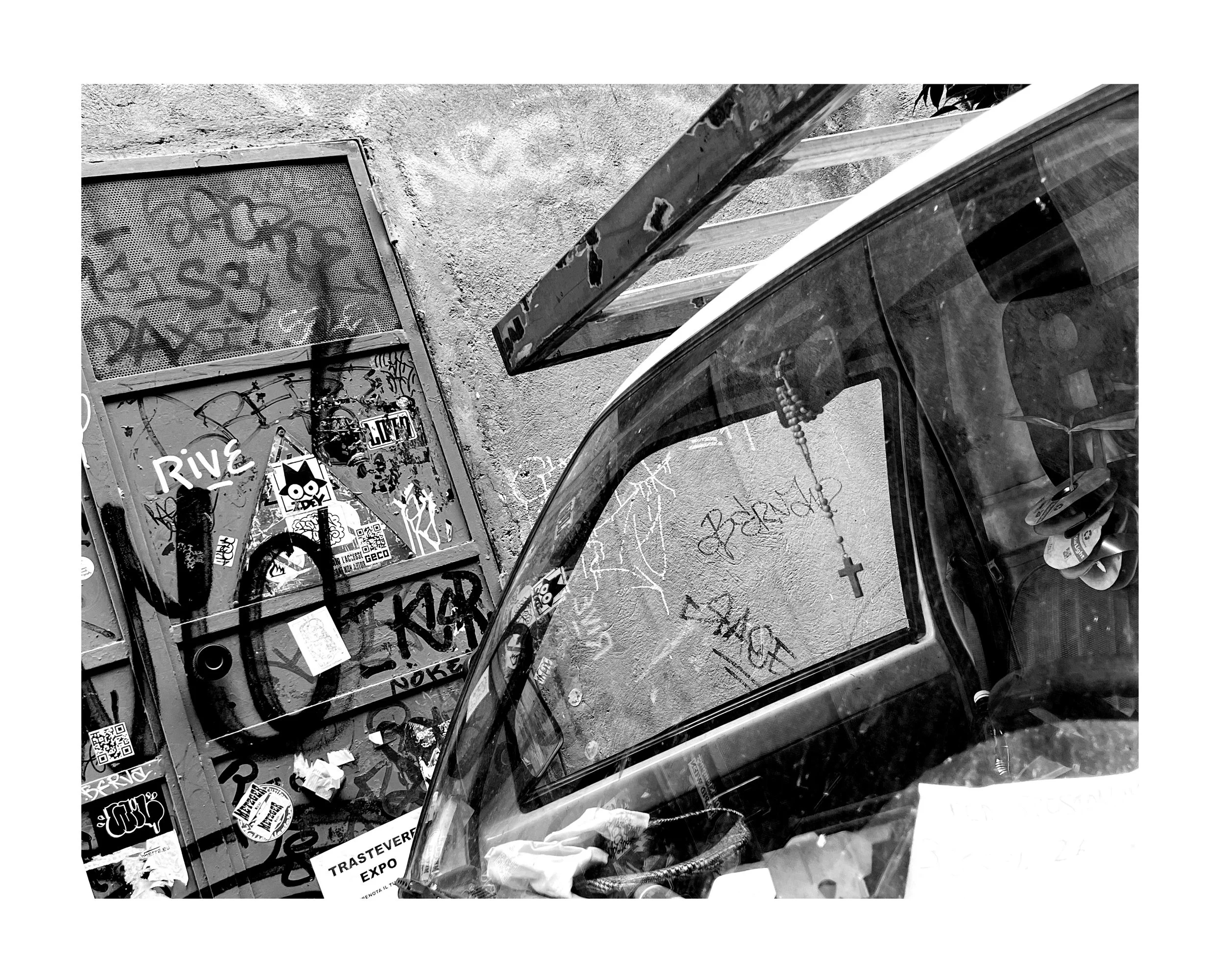 Un parking à vélo, un panneau ou un mur avec des graffitis, une voiture stationnée avec un décor intérieur visible, y compris des objets et une croix suspendue.