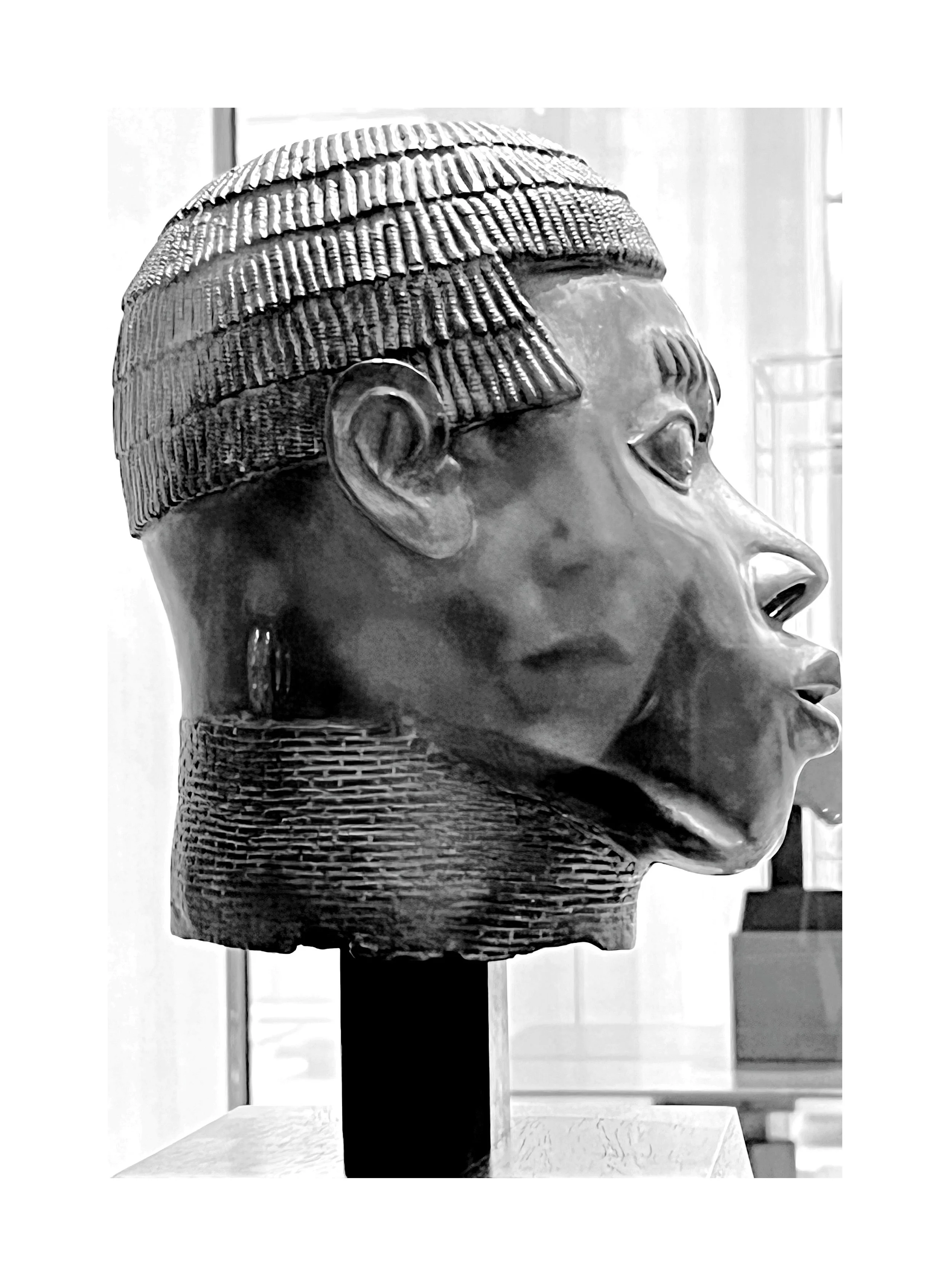 Une sculpture en bronze montrant un profil d'une femme africaine avec des détails dans les cheveux et le visage.