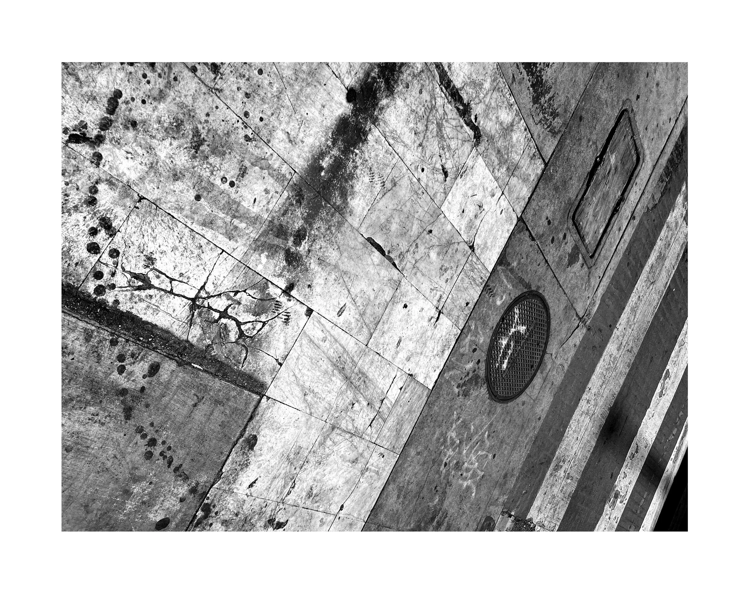 Sol urbain en pavés et béton, avec un regard de drain rond et une grille d'accès, en noir et blanc.