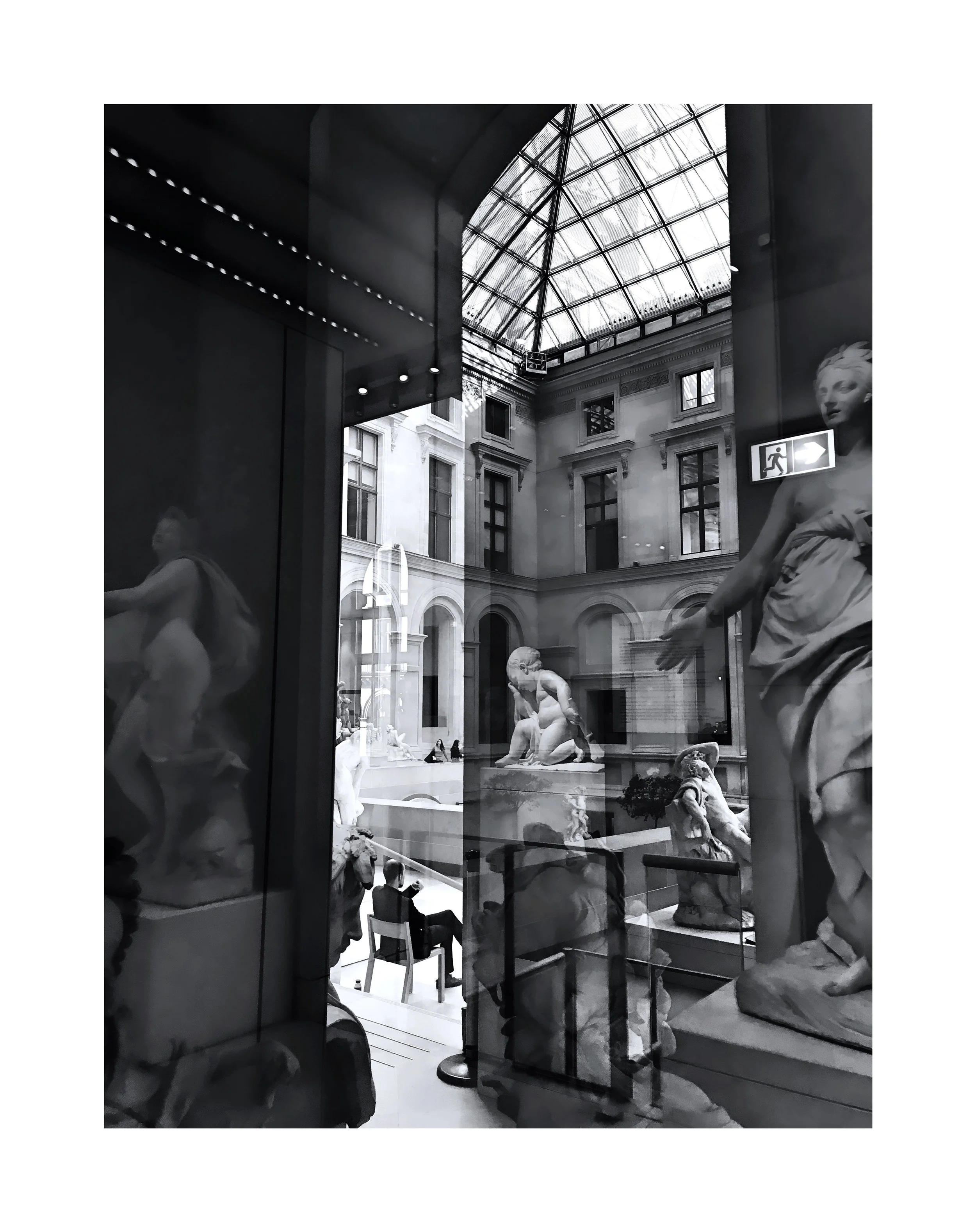 Vue intérieure d'un musée avec de nombreuses sculptures classiques en marbre, un plafond en verre, et des visiteurs qui regardent les œuvres.