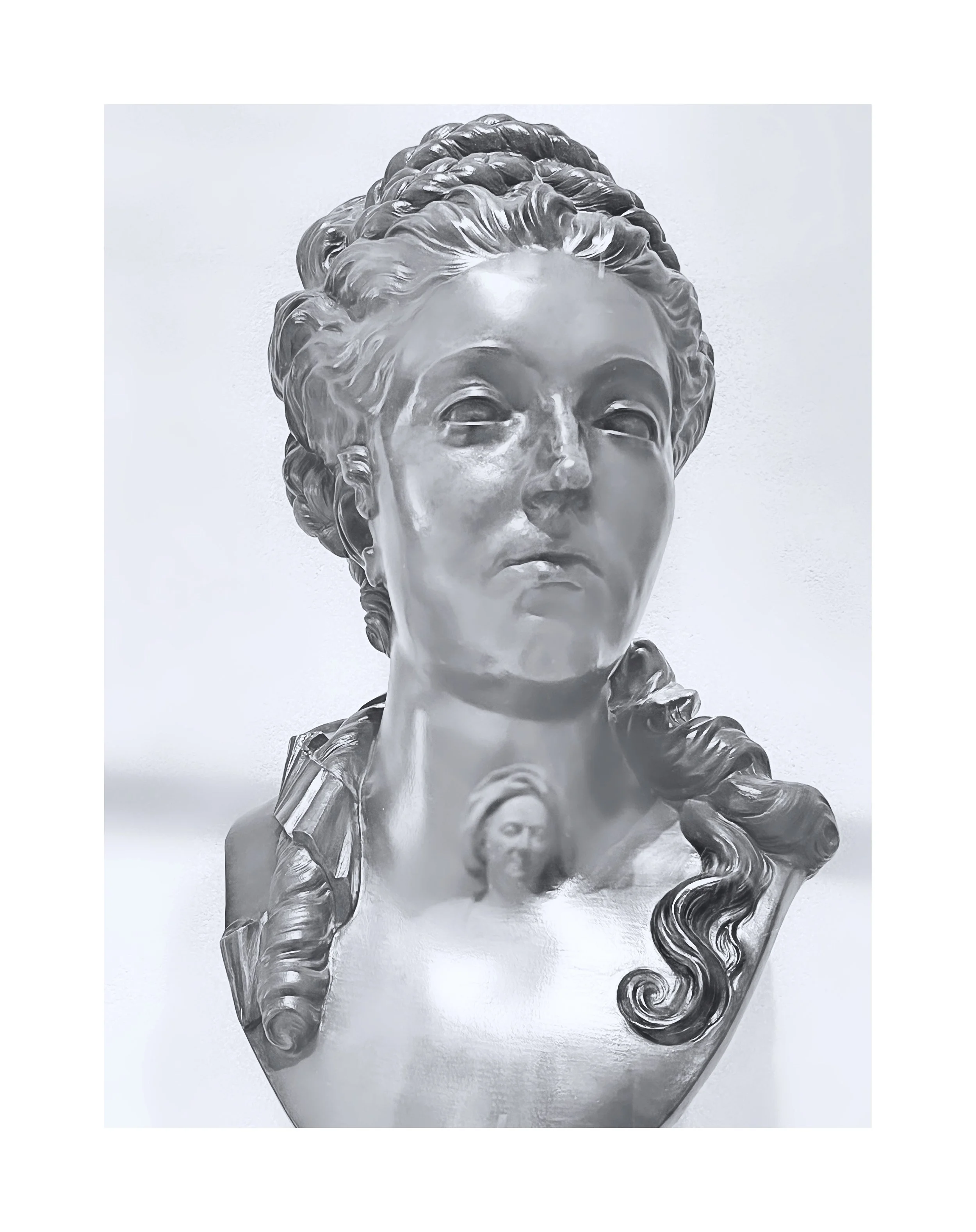 Sculpture en marbre d'une tête féminine avec des cheveux bouclés et une expression sérieuse, accompagnée d'une figurine plus petite en arrière-plan.