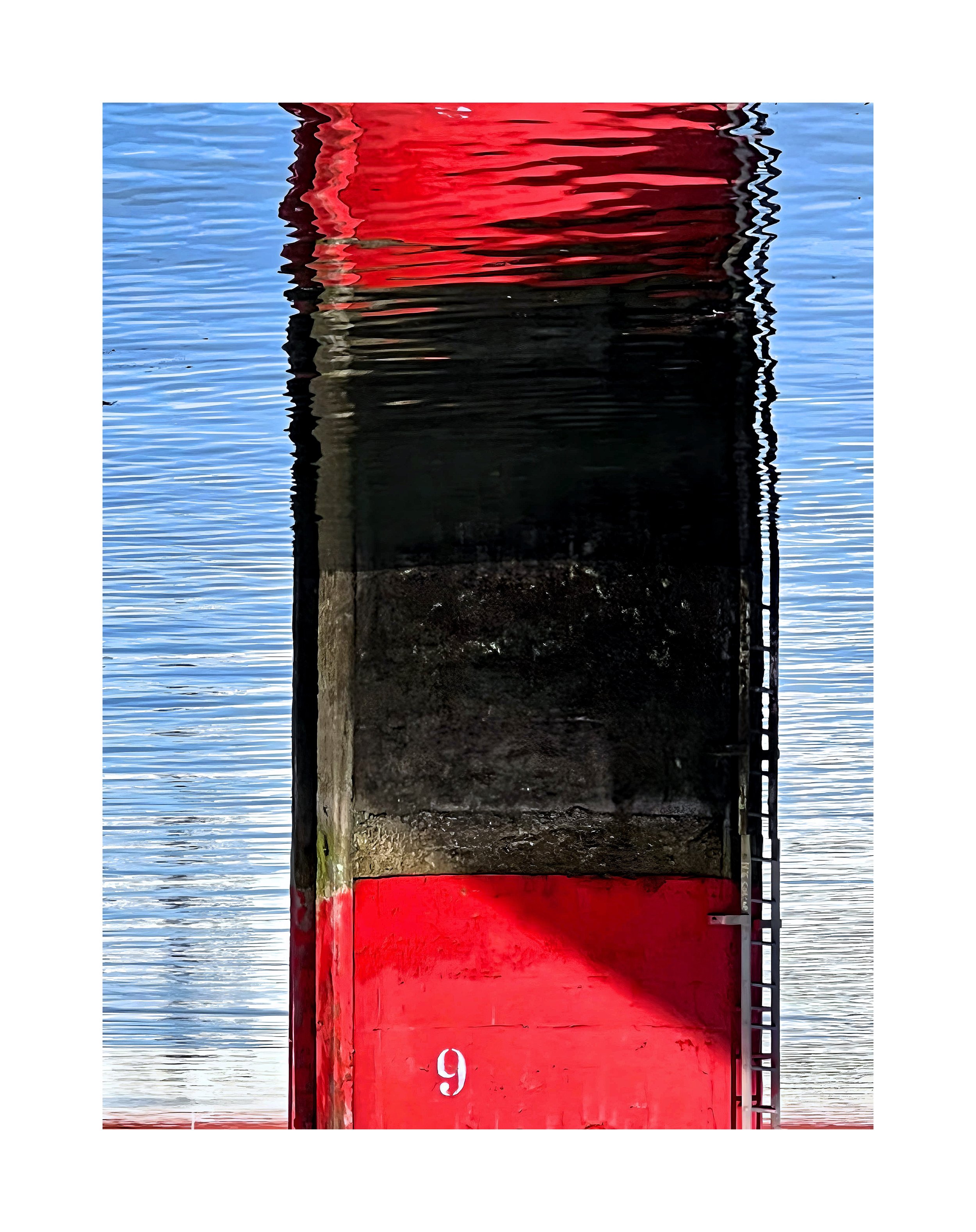 Vue verticale d'une structure en bois ou en métal peinte en rouge avec le chiffre 9, reflétée dans l'eau calme d'un plan d'eau ou d'une mer.