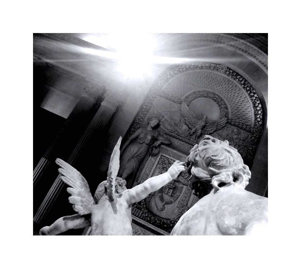 Sculptures en marbre d'un léon et d'une figure ailée dans un musée, avec un fond décoré et une lumière brillante du plafond.