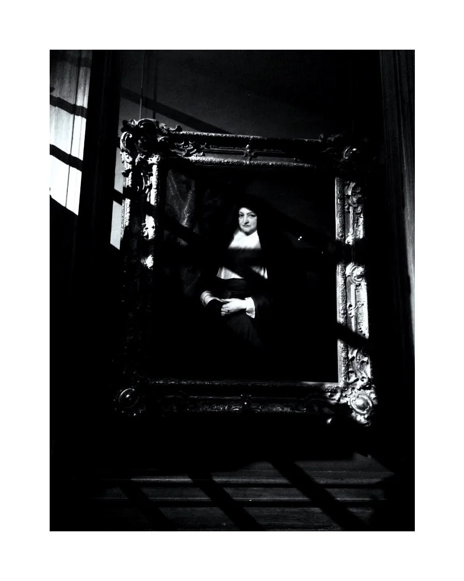 Une peinture en noir et blanc d'une femme habillée en tenues anciennes dans un cadre orné, vue à travers des barres d'escalier en bois.