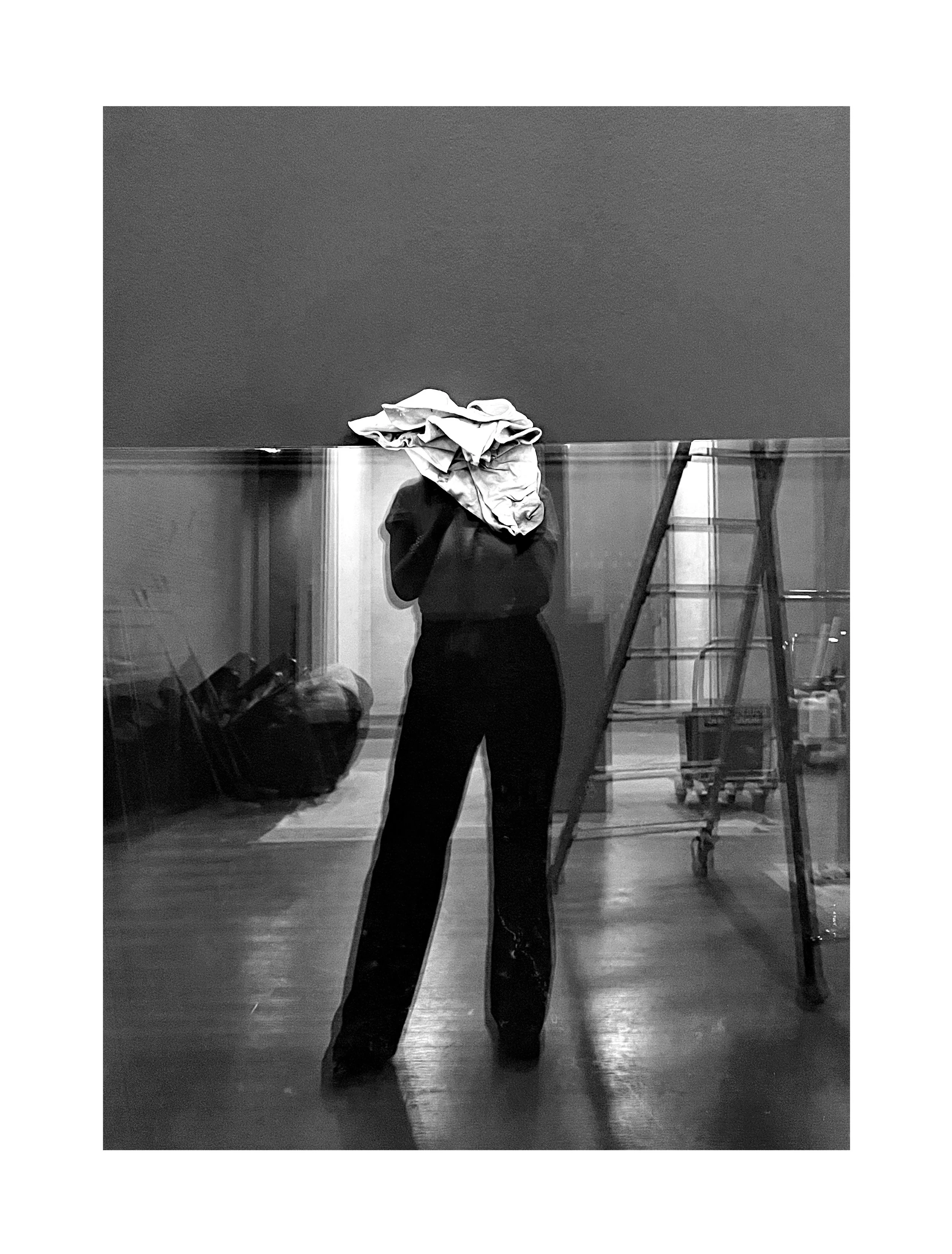 Un reflet d'une personne portant une chemise sur la tête dans un miroir, dans une pièce avec une échelle et des objets de nettoyage.