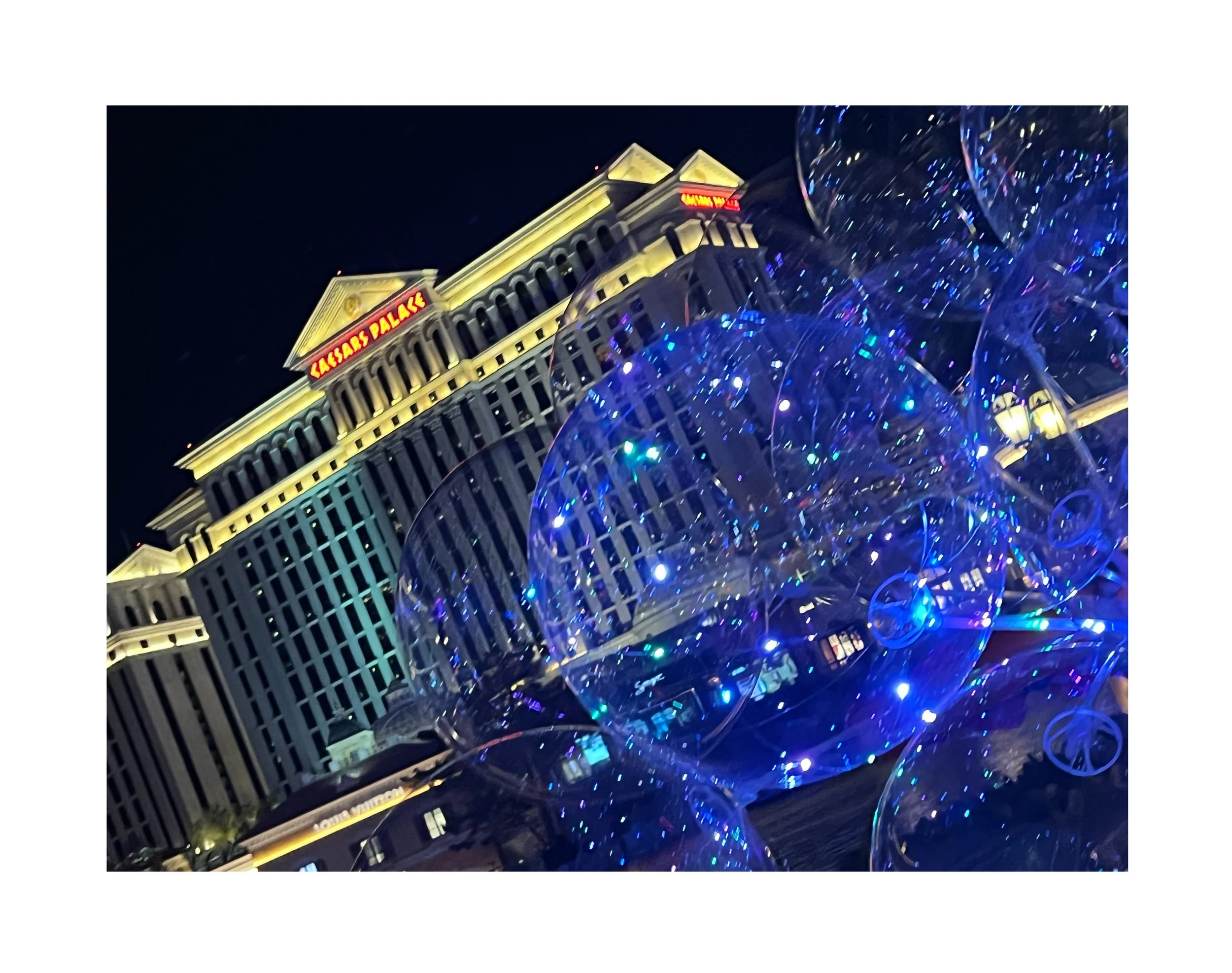 Balles de baudruche en plastique transparent avec des lumières bleues et multicolores, devant le bâtiment Caesars Palace illuminé la nuit.