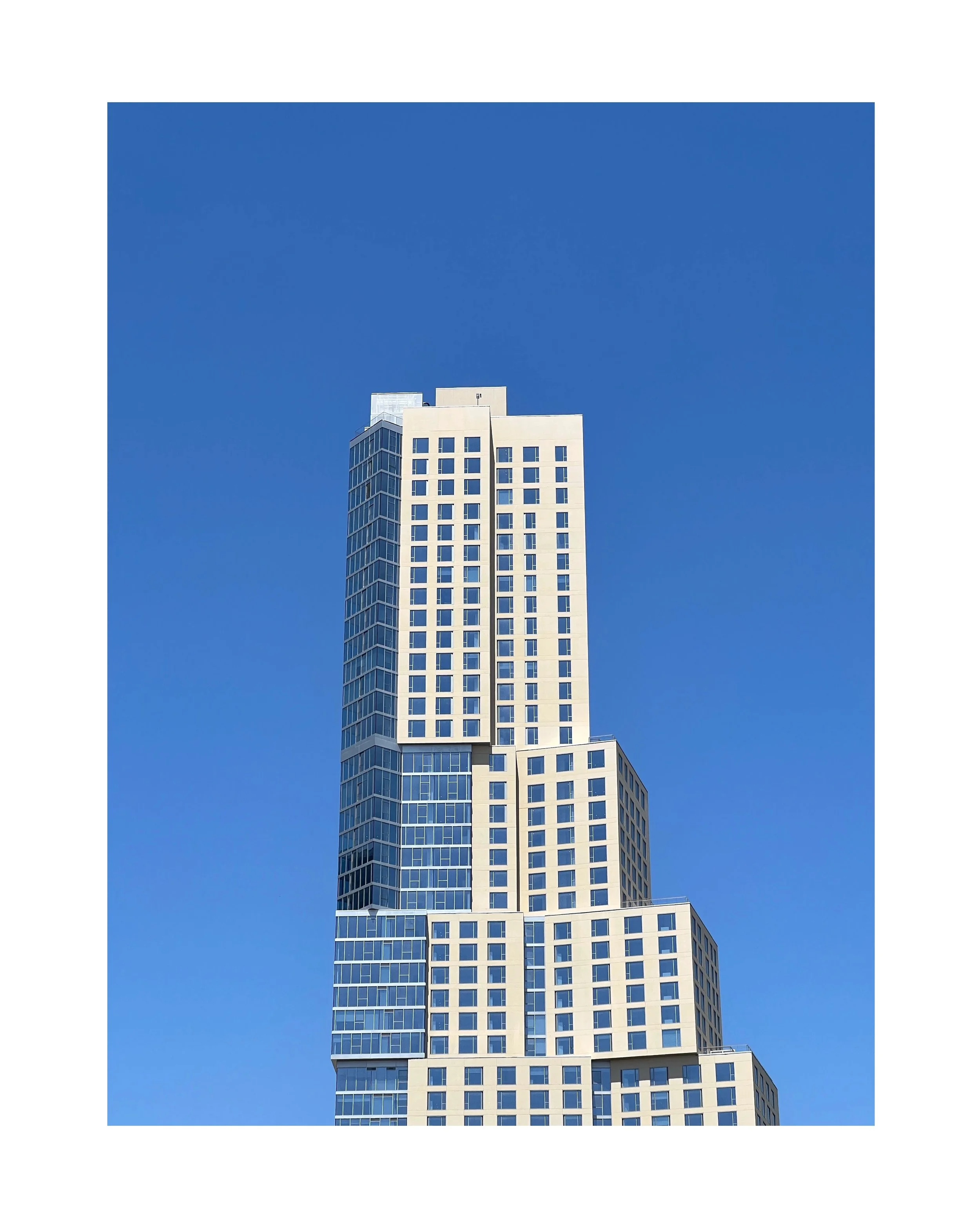 Un gratte-ciel moderne avec une architecture géométrique complexe, composé de plusieurs niveaux décalés, avec une façade en verre et en béton clair, contre un ciel bleu clair.
