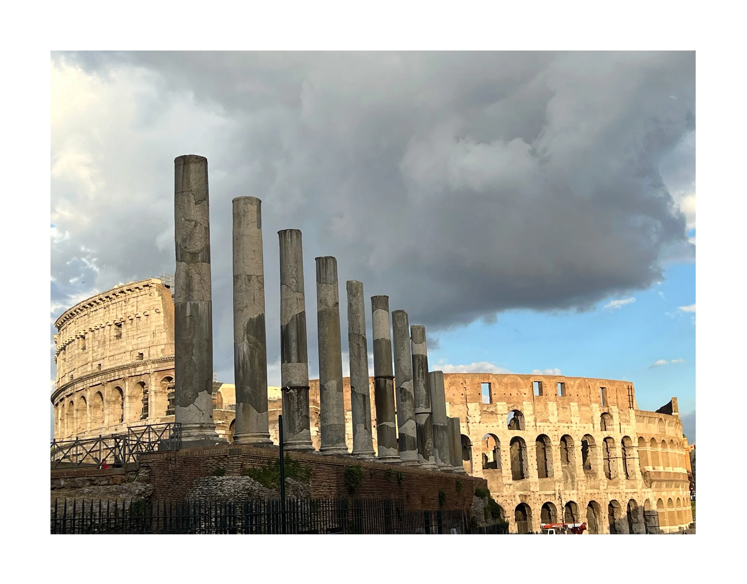 Les ruines du Colisée à Rome avec plusieurs colonnes antiques en premier plan et un ciel nuageux en arrière-plan.